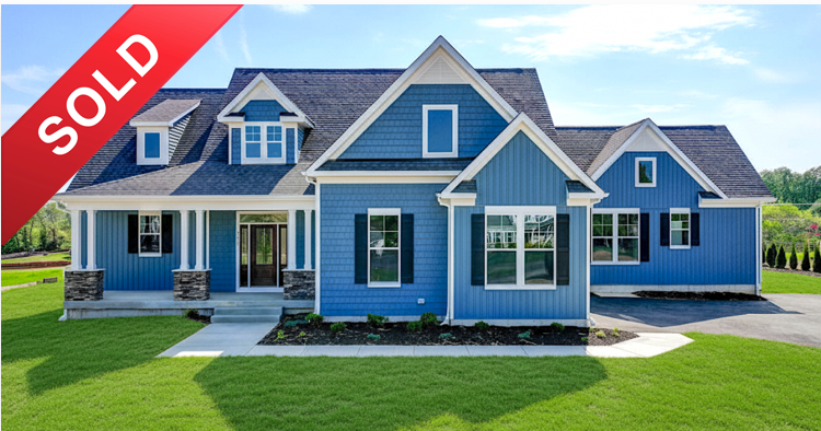 New blue house with a 'SOLD' banner in the top left corner, green front lawn, and a sidewalk leading to the entrance.