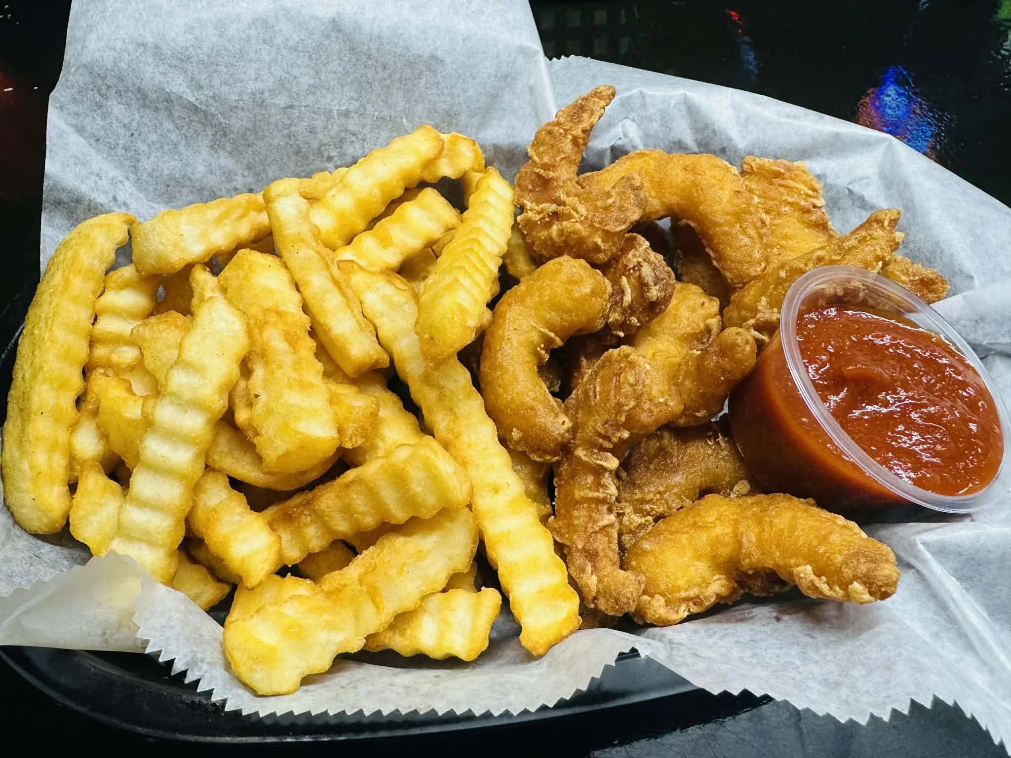 Basket of crinkle-cut French fries and fried chicken tenders with a side of marinara sauce.