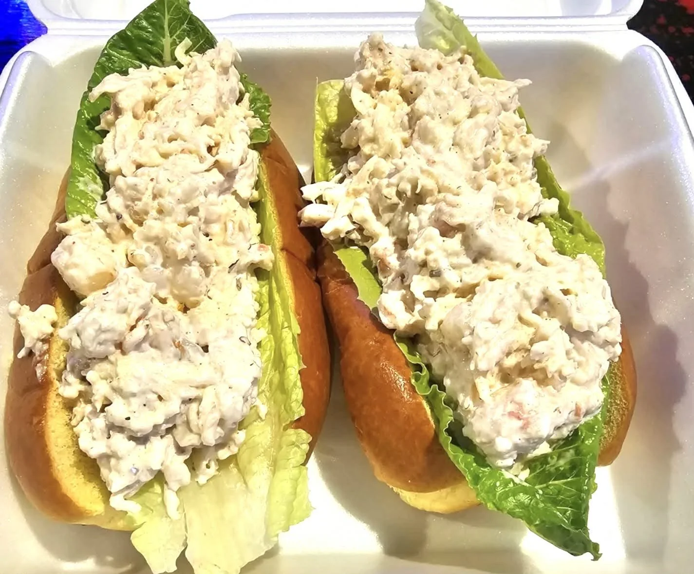 Two fish sandwiches with lettuce in a foam container.