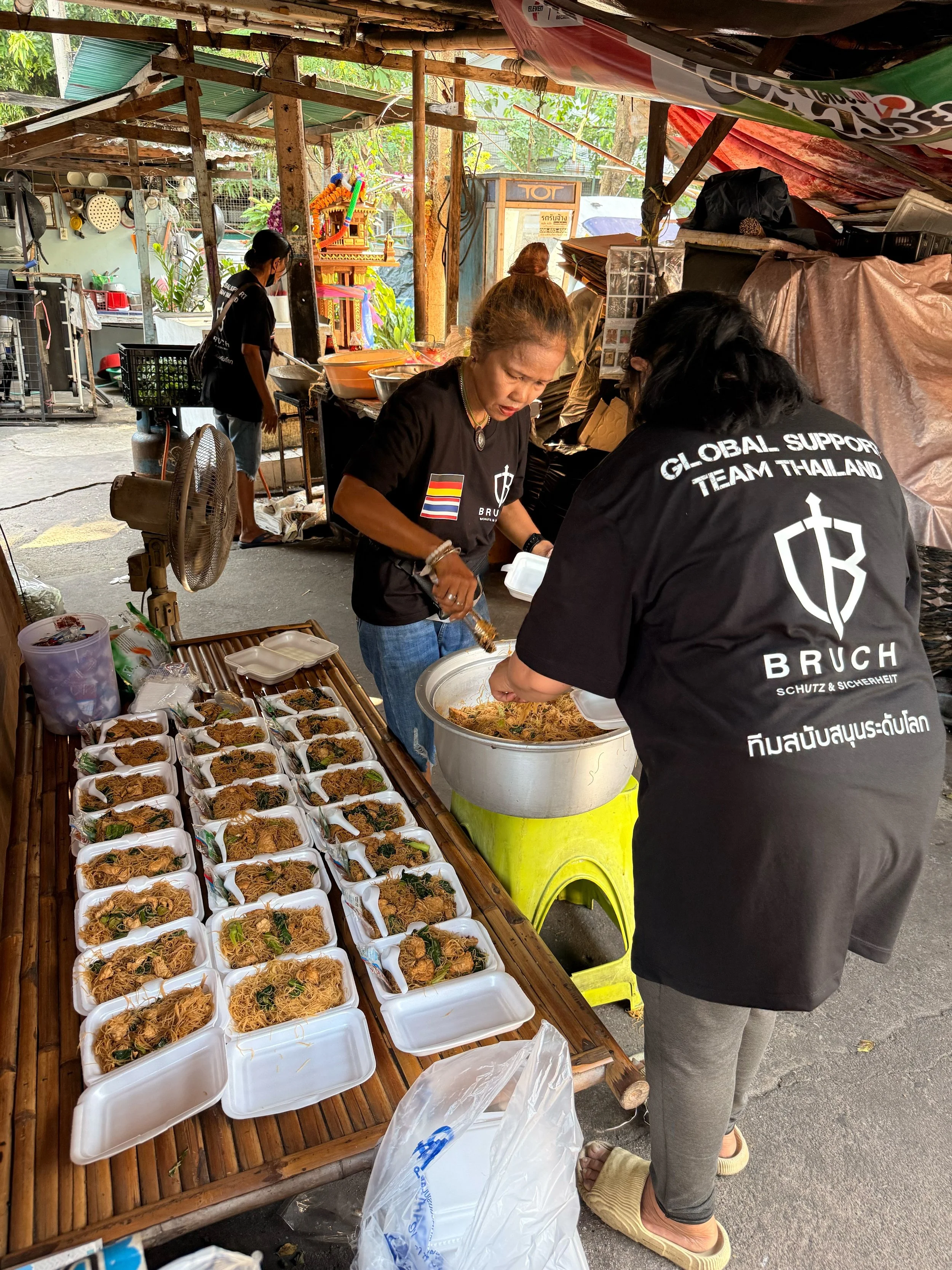 Menschen, die thailändisches Essen in einem Straßenmarkt zubereiten und verkaufen, mit gefüllten Nudelboxen auf einem Holztisch.