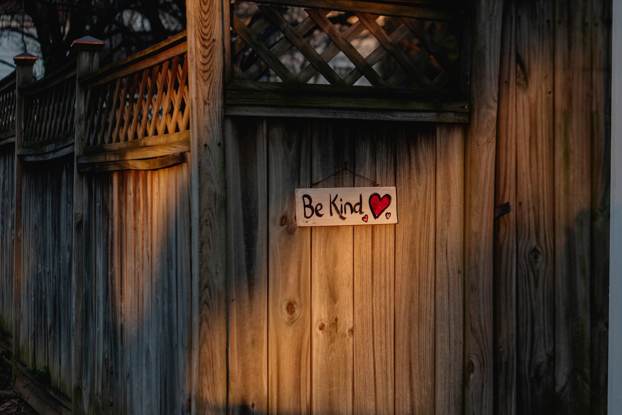 A hand-painted sign on a wooden fence that reads "Be Kind" with hearts on it