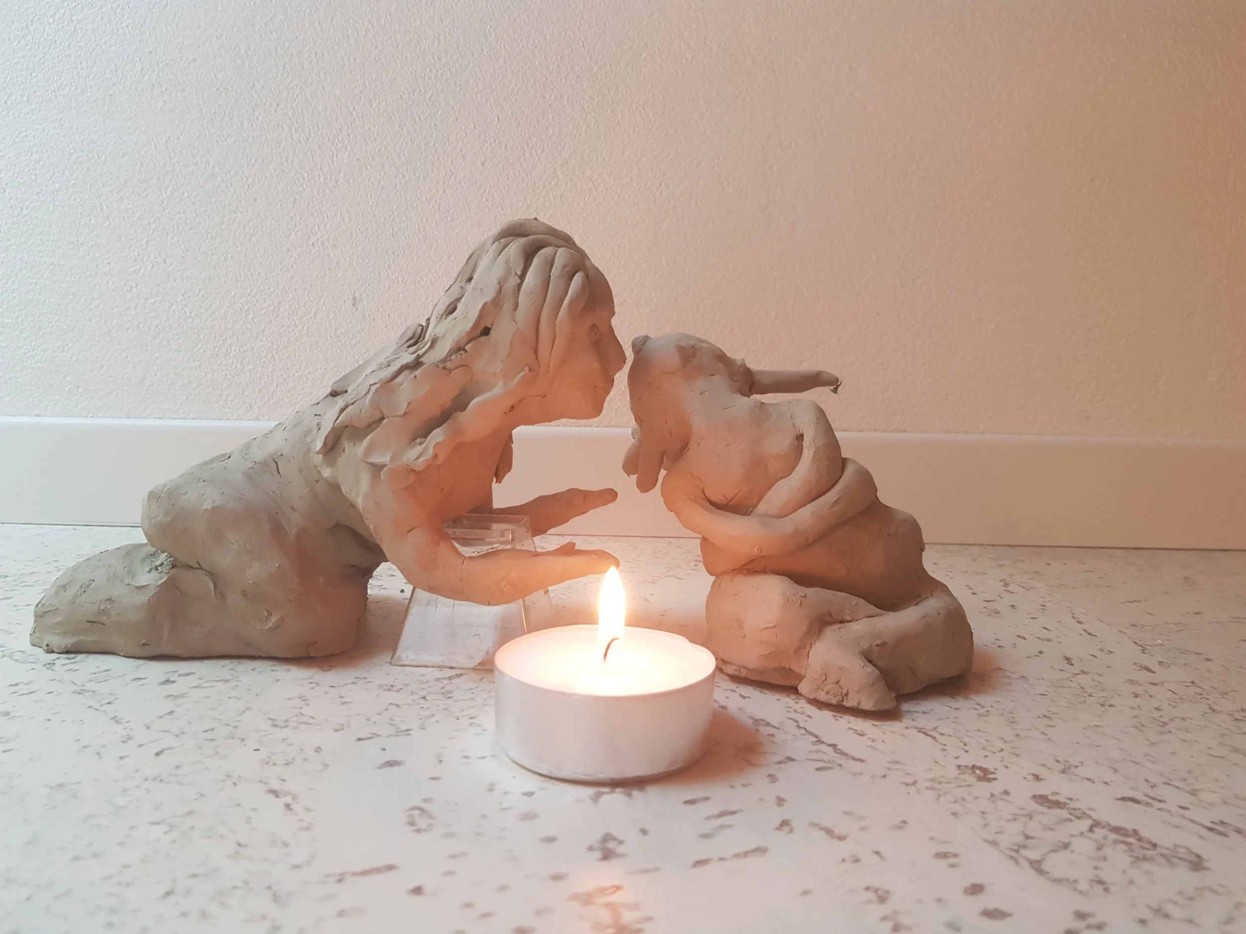 Clay sculptures of a woman and a boy with a lit candle in front of them