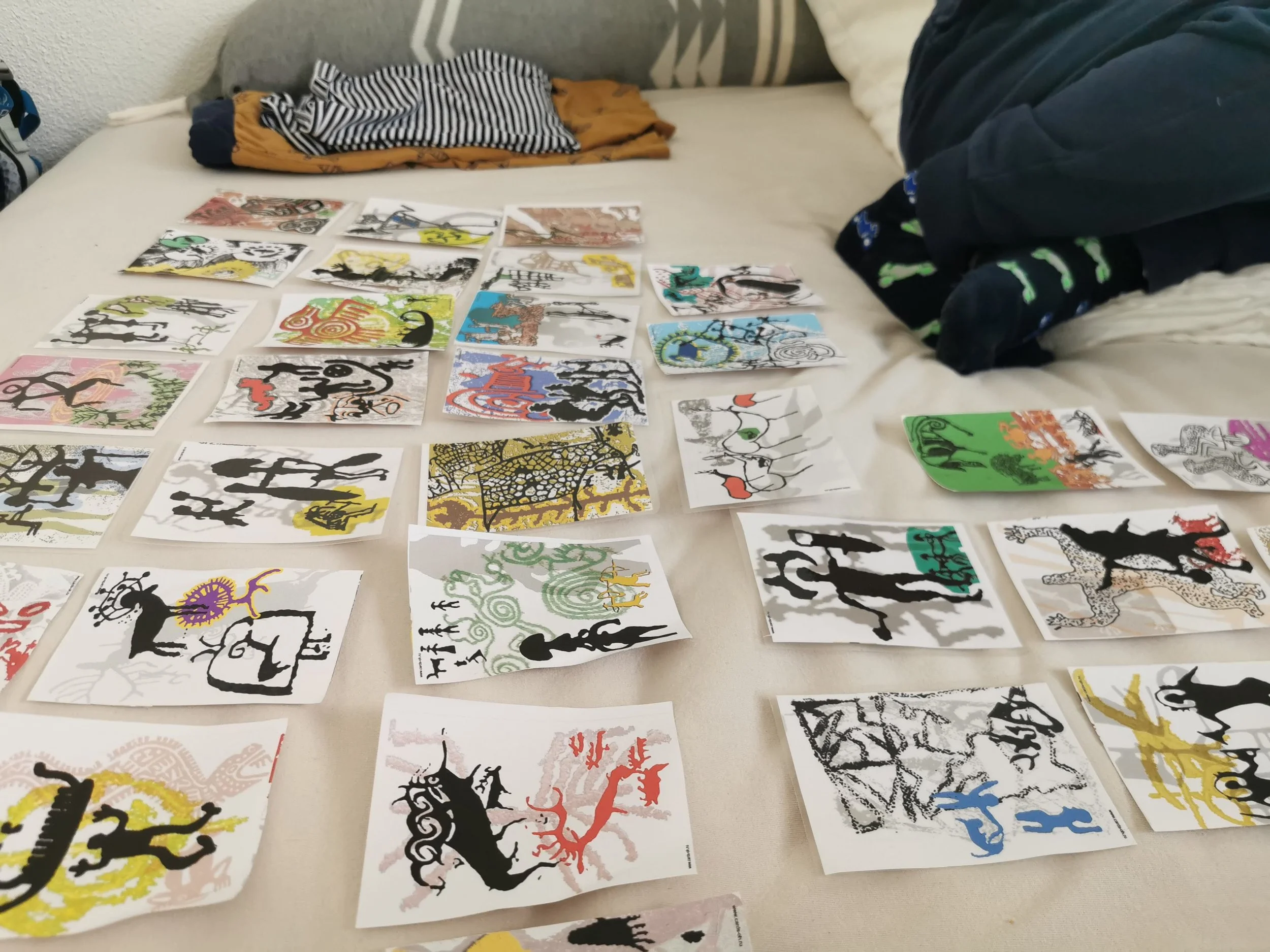 Colorful cards depicting various animal silhouettes, arranged on a bed with some clothing and a pillow nearby.