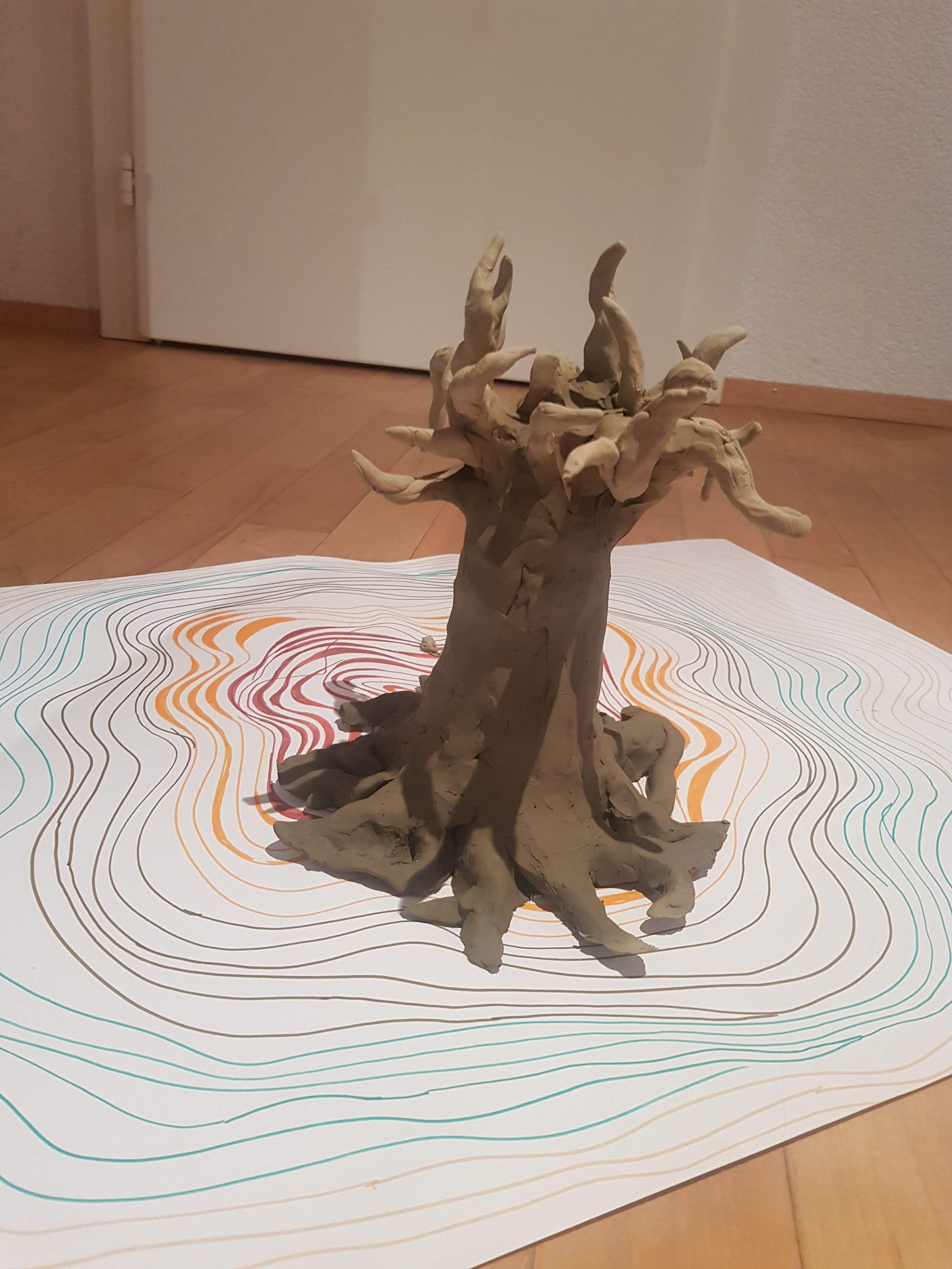 Clay sculpture of a tree with twisting branches, placed on top of a colorful, contoured paper.