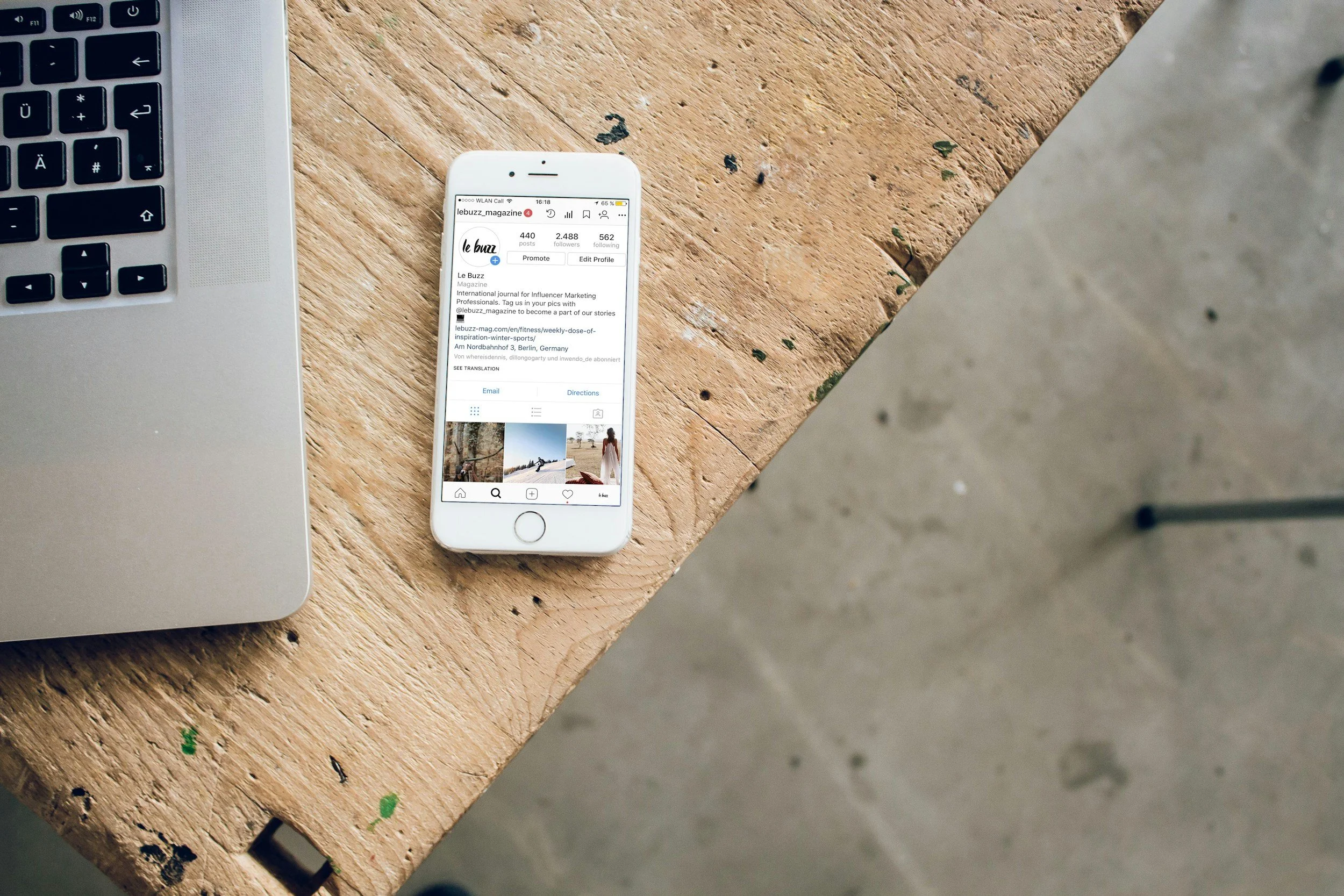 A laptop and an iPhone on a wooden table, with the Phone displaying an Instagram profile.