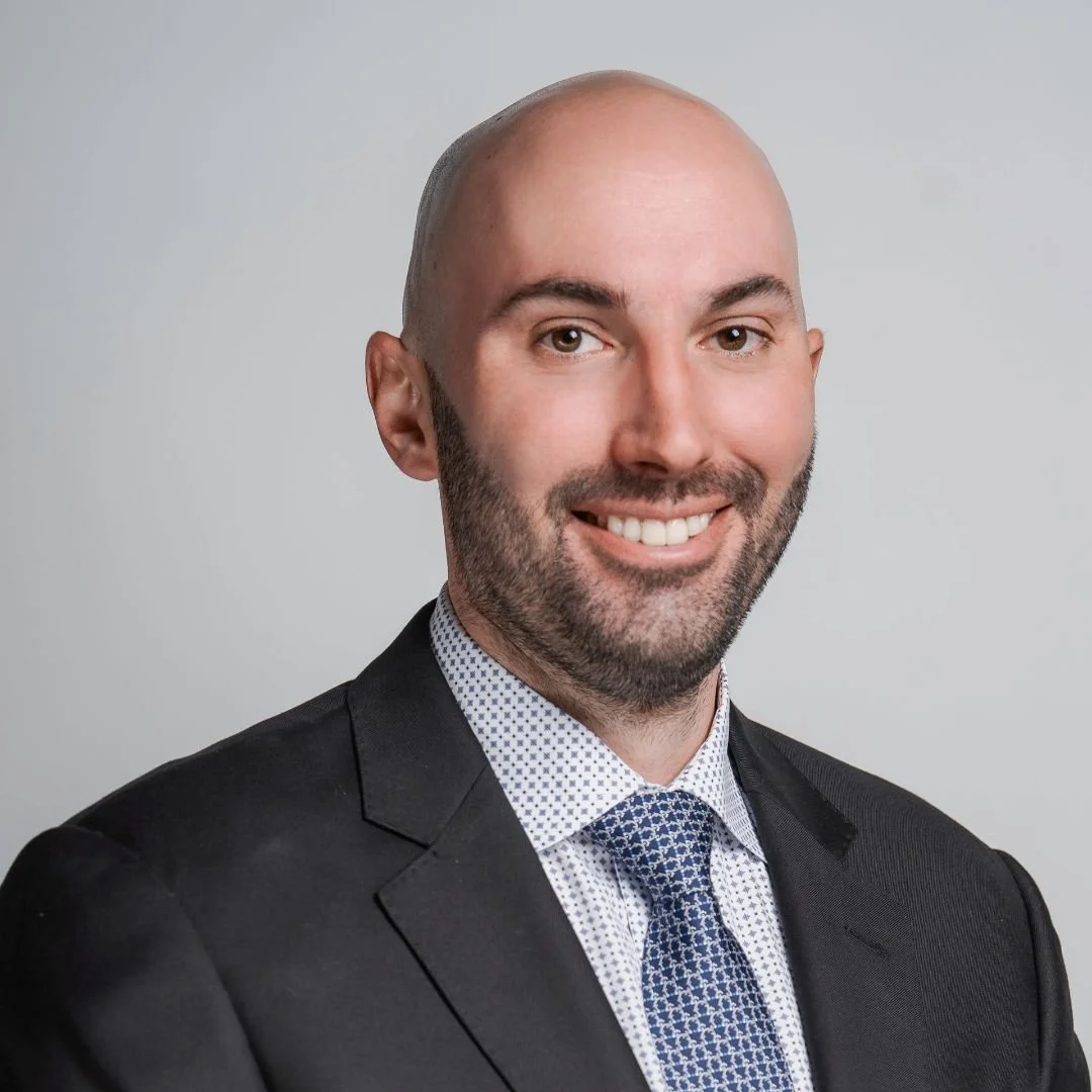 Professional headshot of a smiling man in a suit and tie against a plain background.