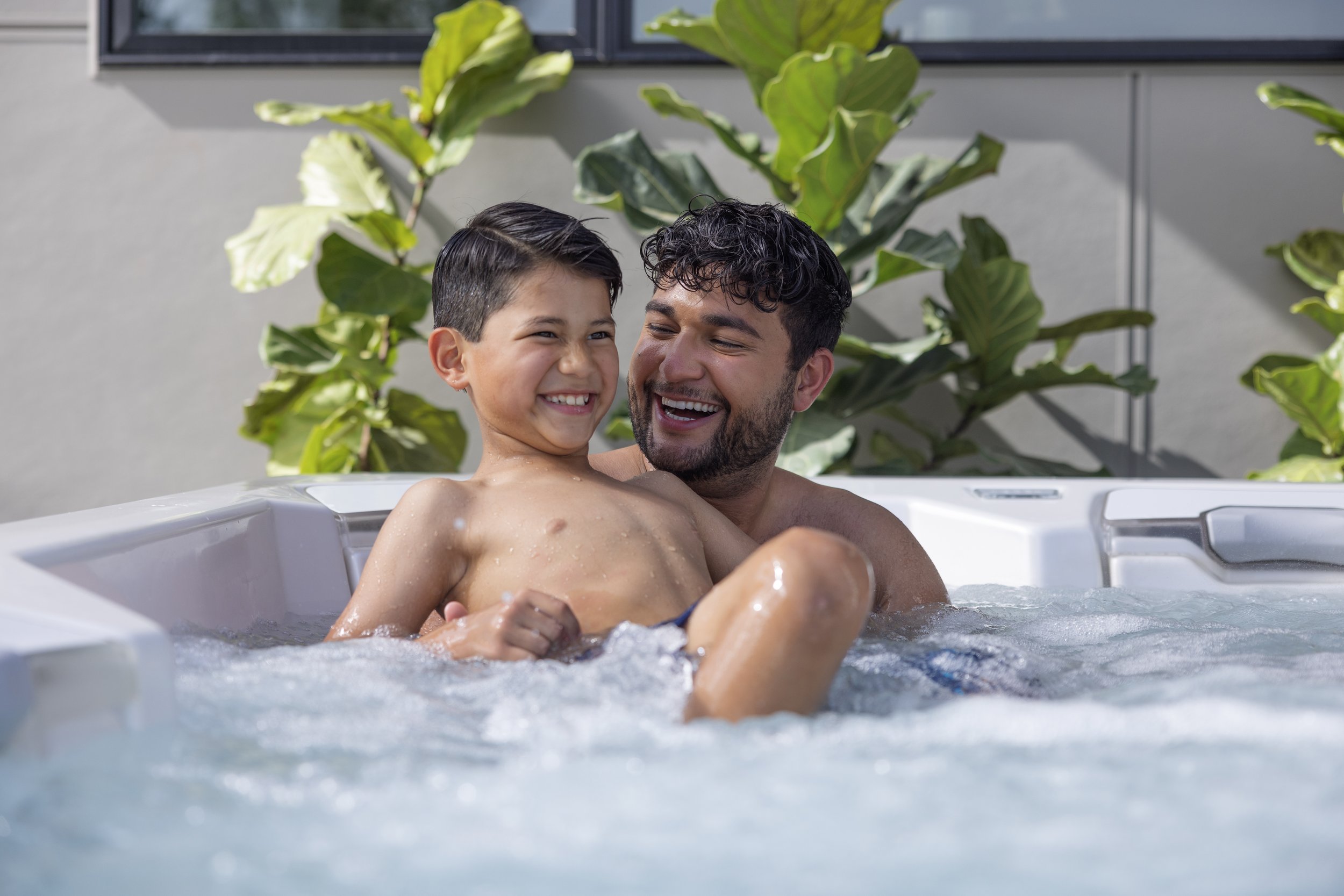 A man and a young boy enjoying time together in a hot tub outdoors, smiling and laughing.