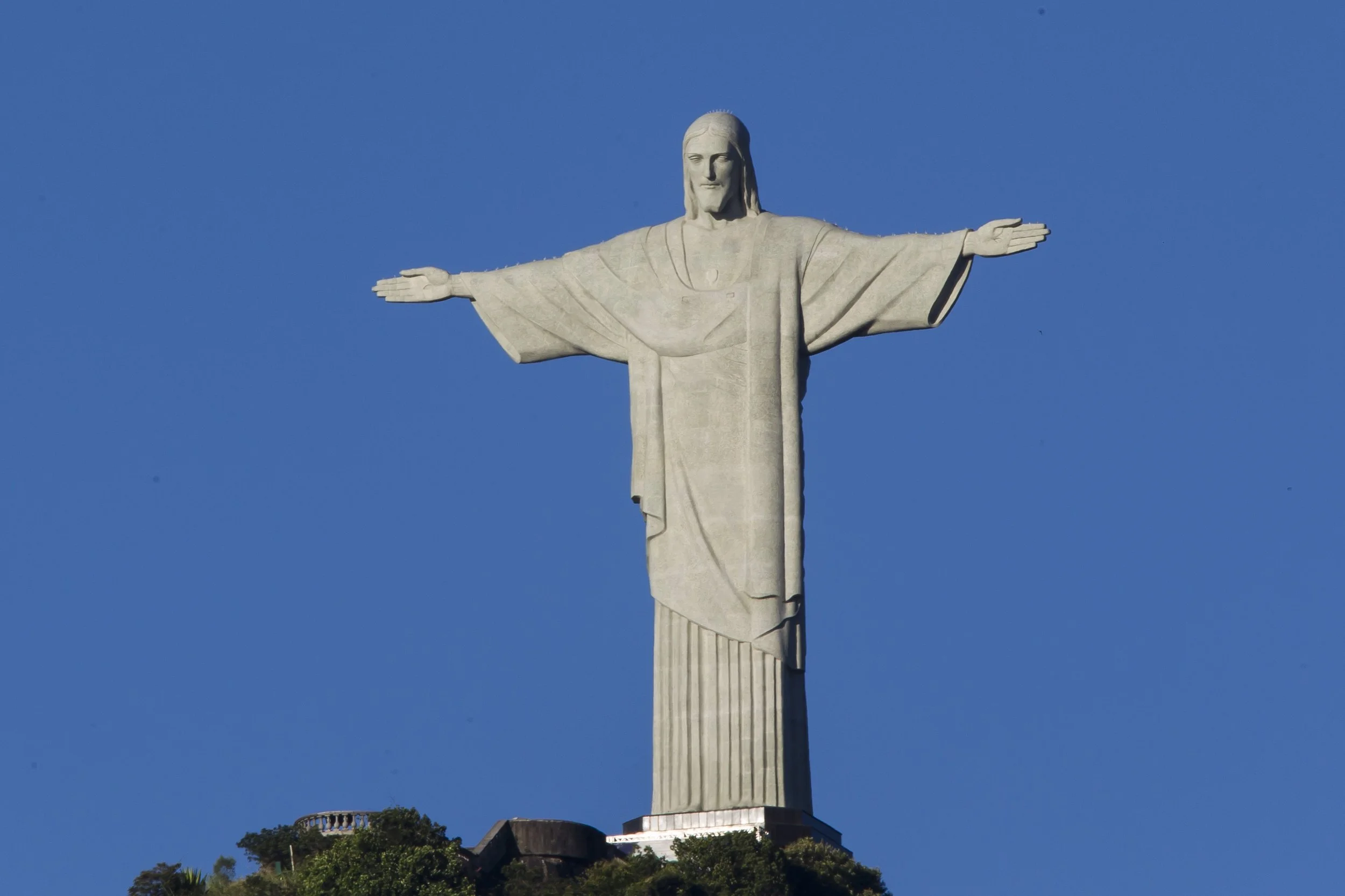 The Christ the Redeemer statue with open arms stands tall against a clear blue sky, overlooking the city and greenery below.