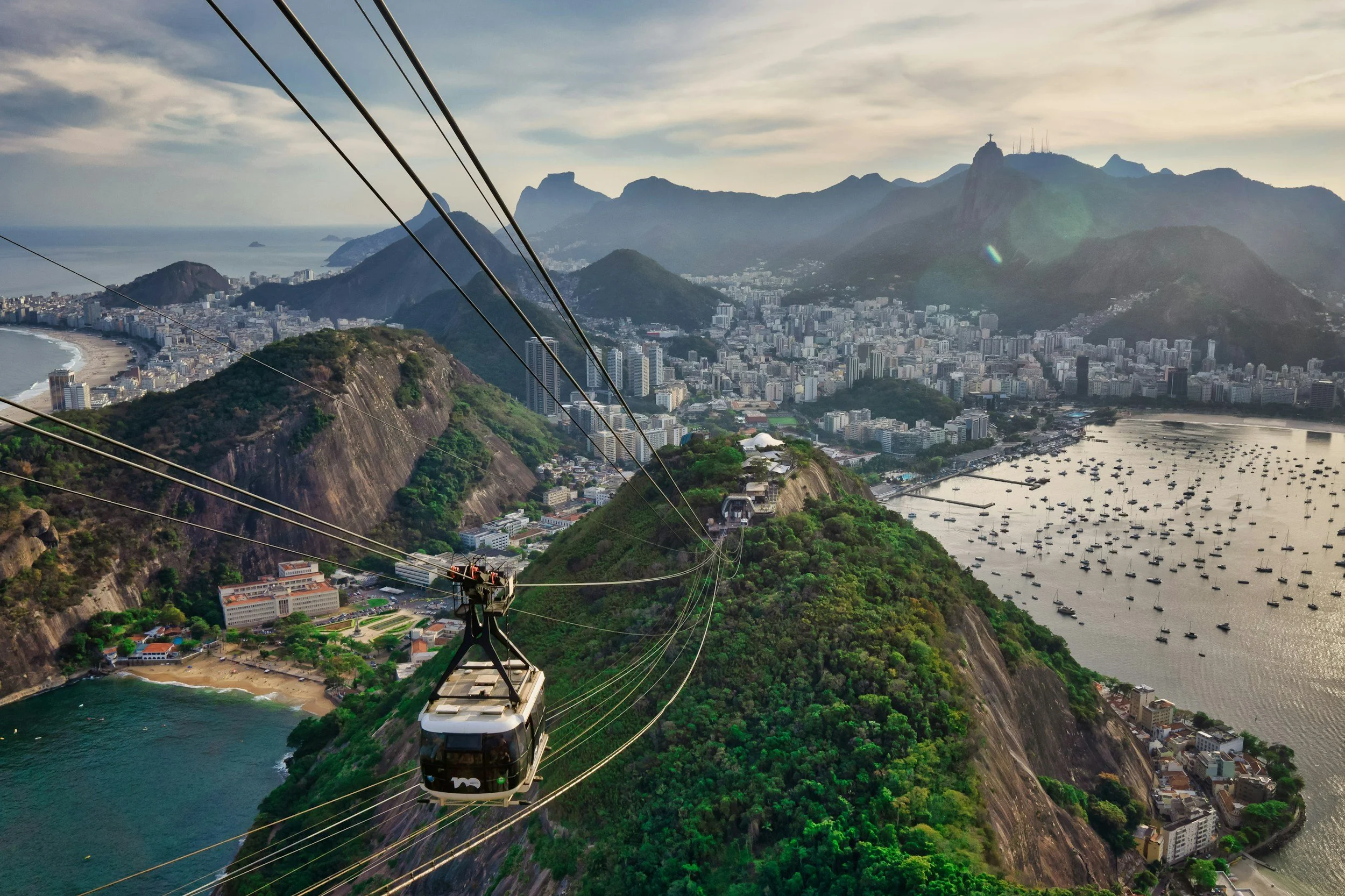 A cable car ascending Mount Corcovado with the Christ the Redeemer statue visible on the mountain top in Rio de Janeiro, Brazil, overlooking the city, ocean, and surrounding mountains.