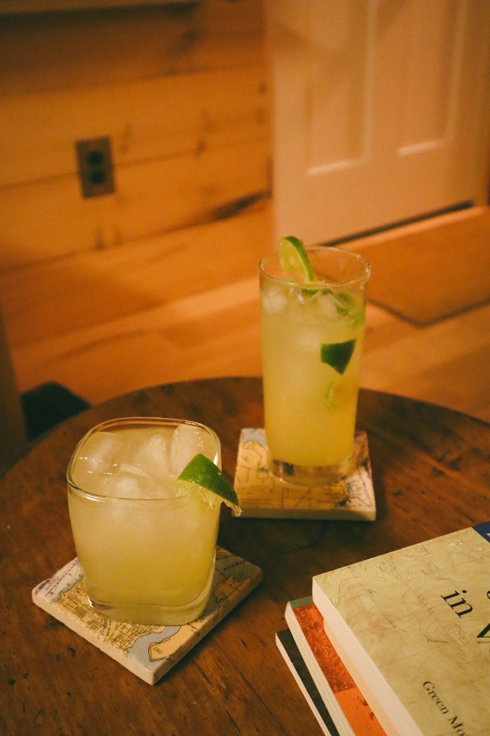 Two glasses of lemonade with lime slices and ice on a wooden table, with a book nearby.