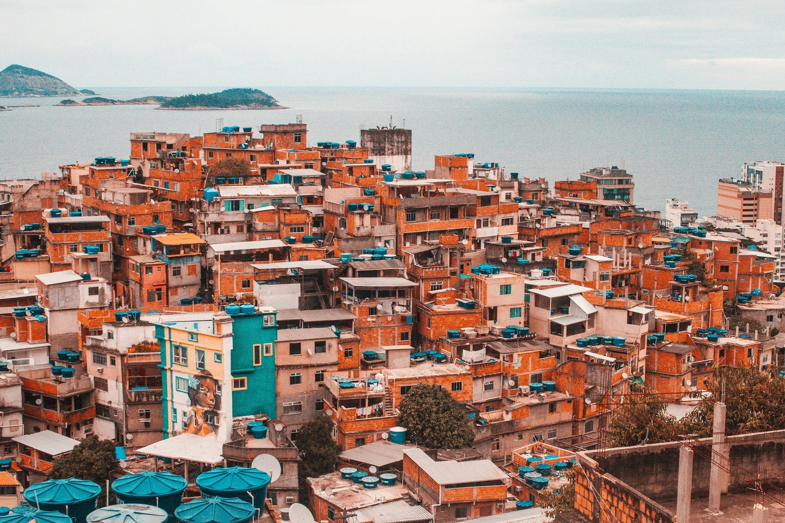 A densely packed cityscape with numerous brick buildings topped with blue water tanks, overlooking a body of water with small islands in the background.