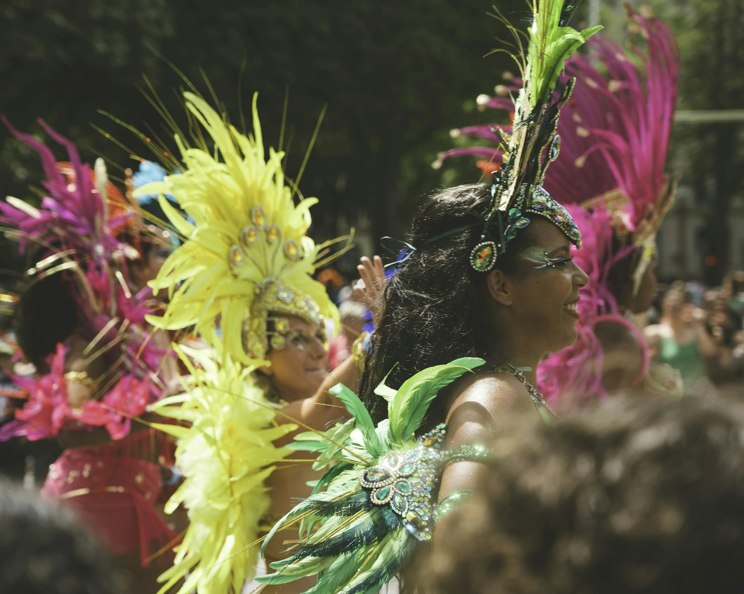Women participating in a parade wearing colorful costumes with feathers and sequins.