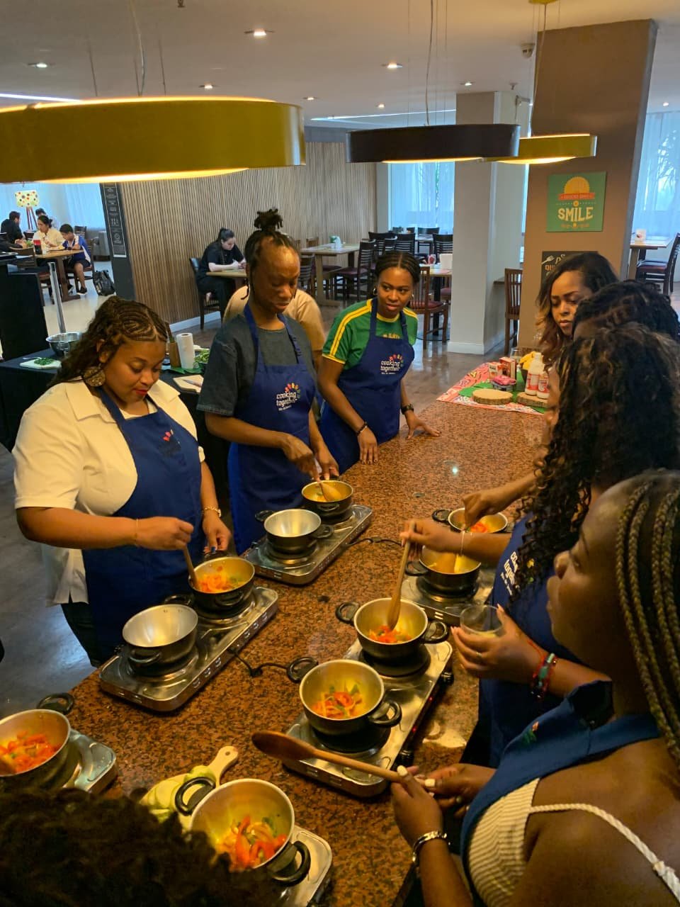 Group of women cooking and stirring soups on portable stoves in a cooking class or workshop setting.
