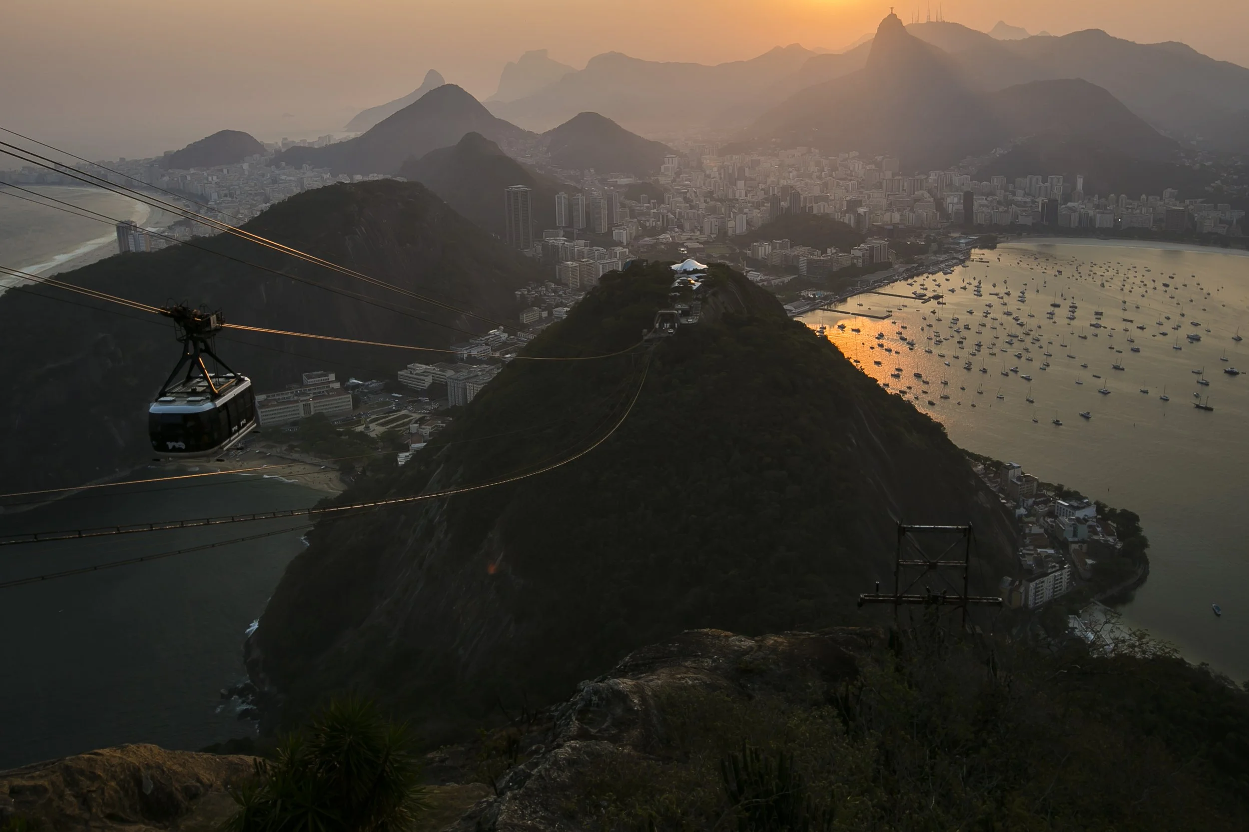 A cable car ride over mountains and a city at sunset, with boats anchored in a bay.