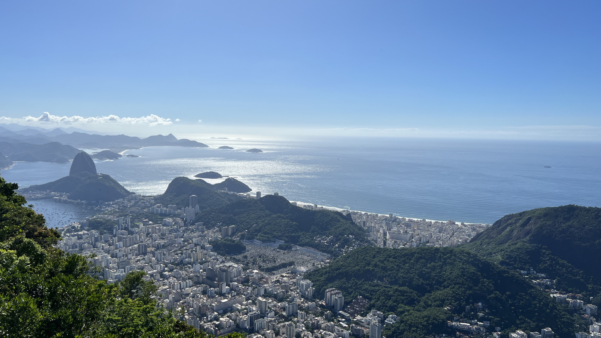 A panoramic view of Rio de Janeiro with Sugarloaf Mountain, the city, and the Atlantic Ocean in the background under a blue sky.