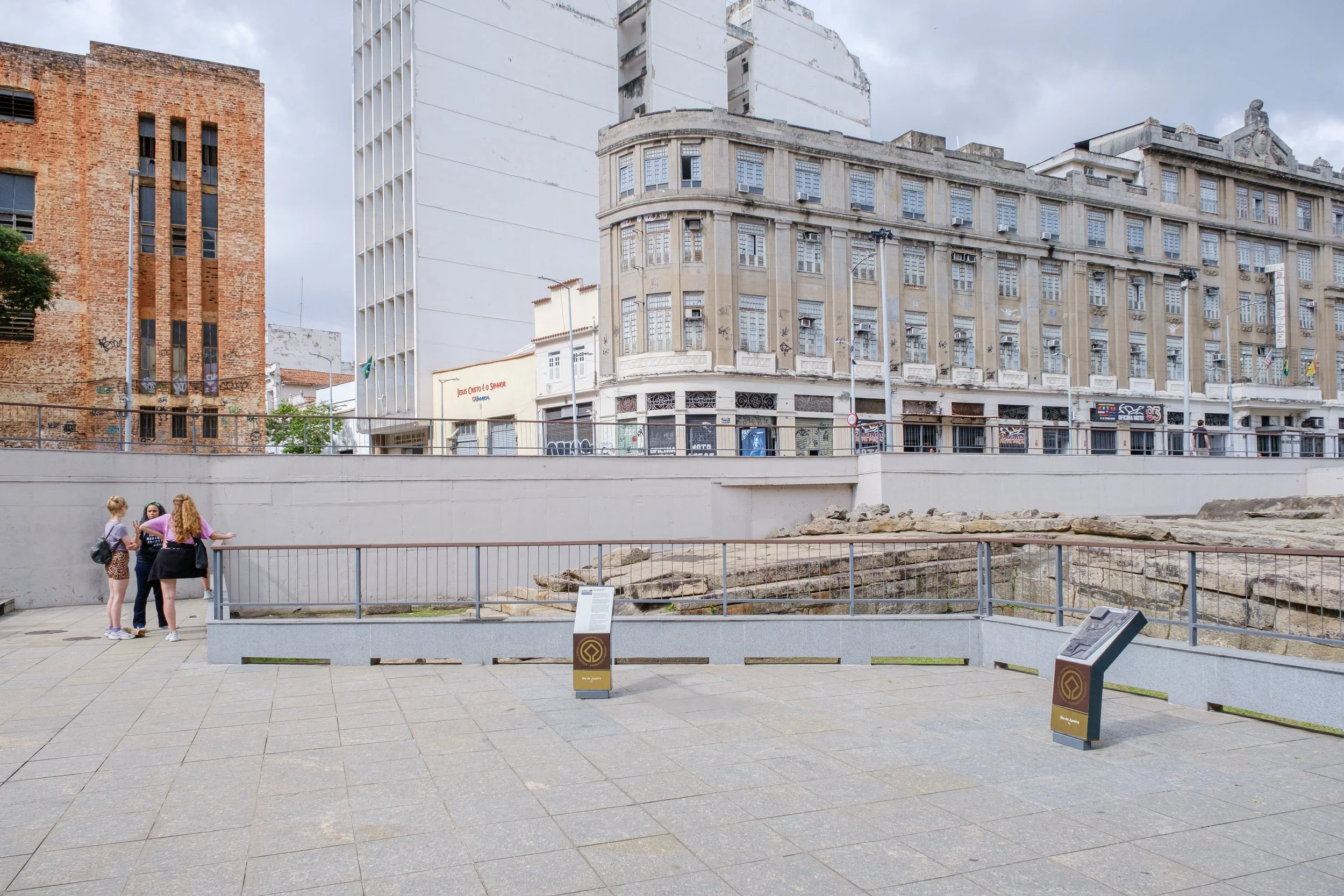 Group of four women standing and talking in an outdoor urban area with old buildings in the background.