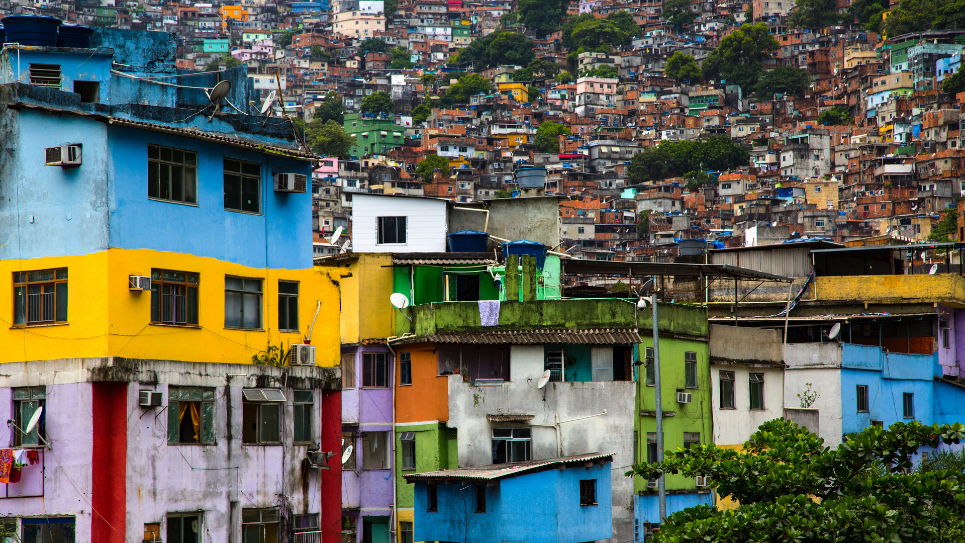 Colorful hillside neighborhood with various painted houses, some with satellite dishes, and a dense backdrop of similar houses on the slope