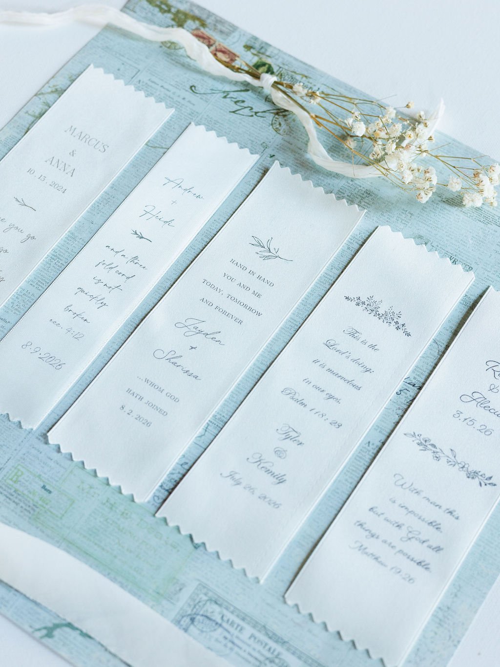 A display of wedding invitations and RSVP cards arranged on a blue patterned surface with a small bouquet of white baby's breath flowers placed on top.