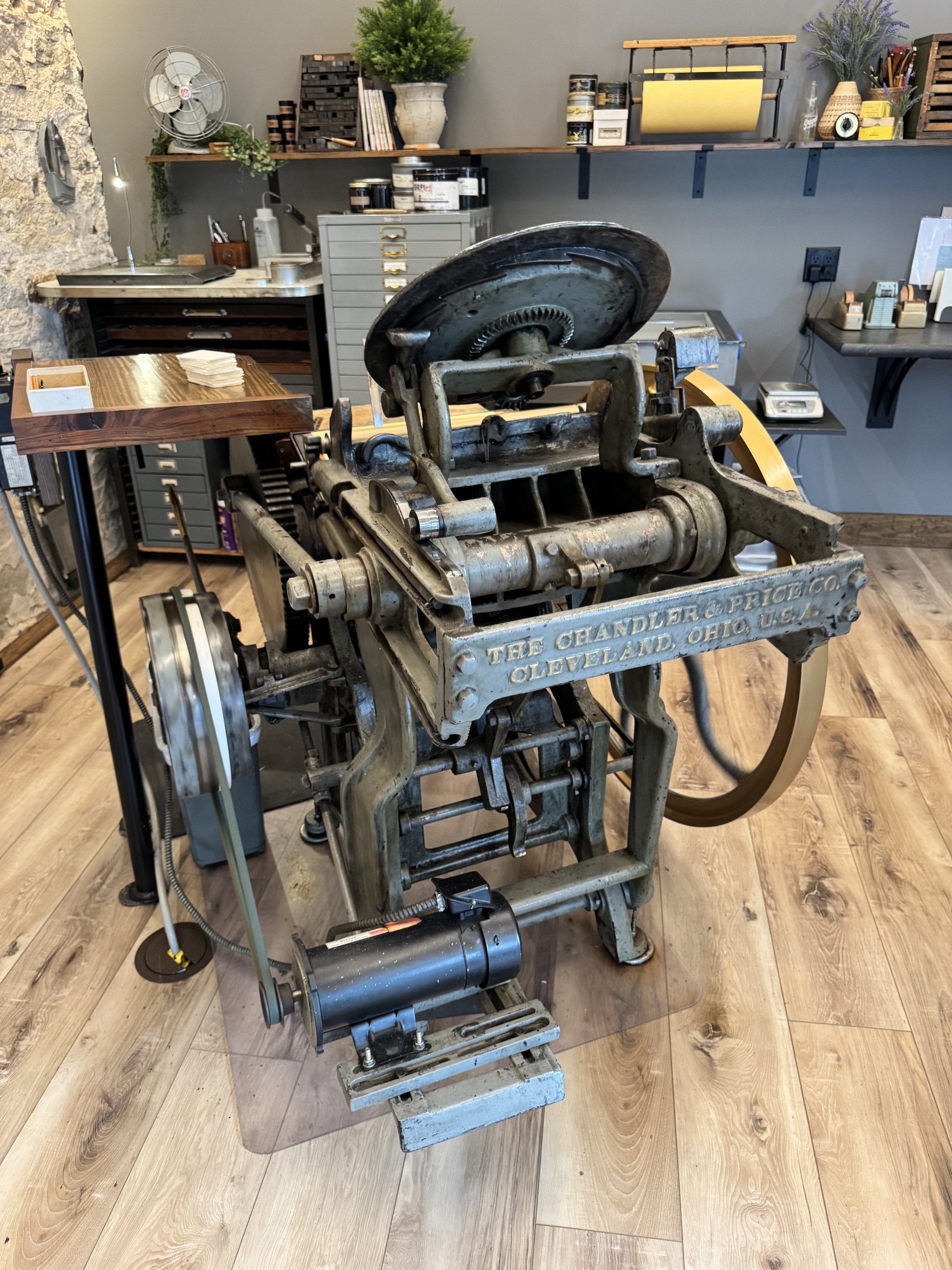 Vintage metal machine in a workshop with shelves, plants, and tools in the background.