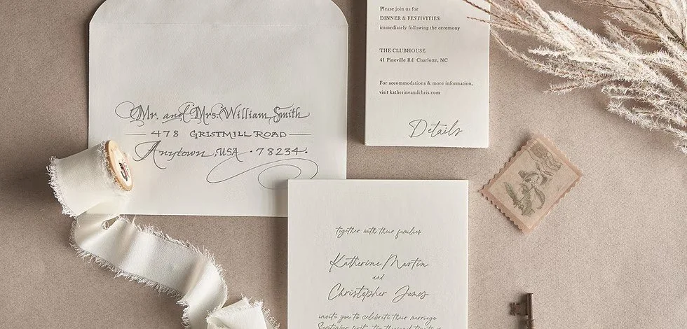 Wedding invitation suite with RSVP card, envelope addressed to Mr. and Mrs. William Smith, vintage postage stamp, spool of white ribbon, dried foliage, and small antique key on a neutral background.