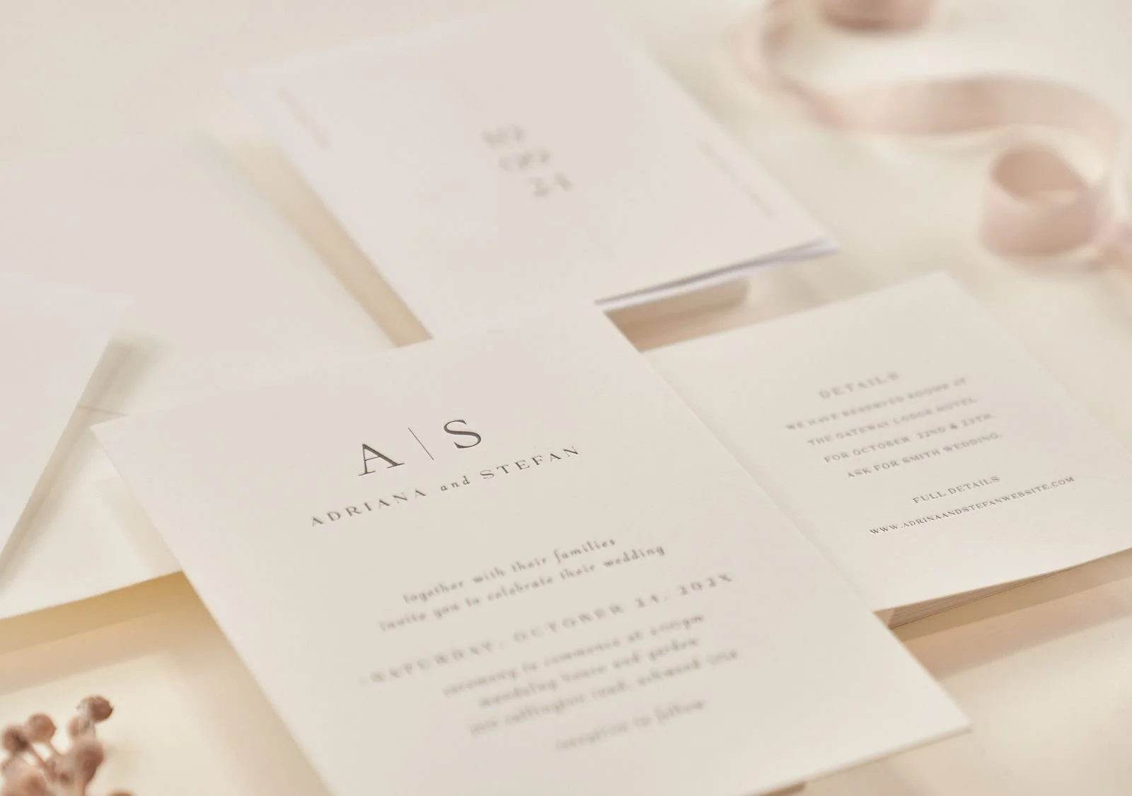 Wedding invitation cards for Adriana and Stefan with elegant minimalist design, laid on a white surface with some pink decorative items nearby.