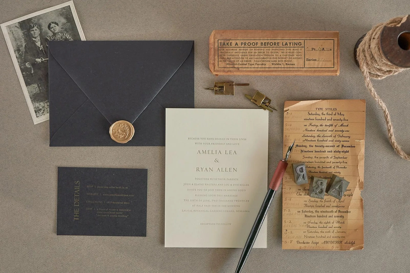 A wedding invitation ensemble with vintage and handwritten elements, including a navy blue envelope with a wax seal, a black RSVP card, a white wedding invitation, a black speech bubble note with online RSVP details, old handwritten date notes, a typ