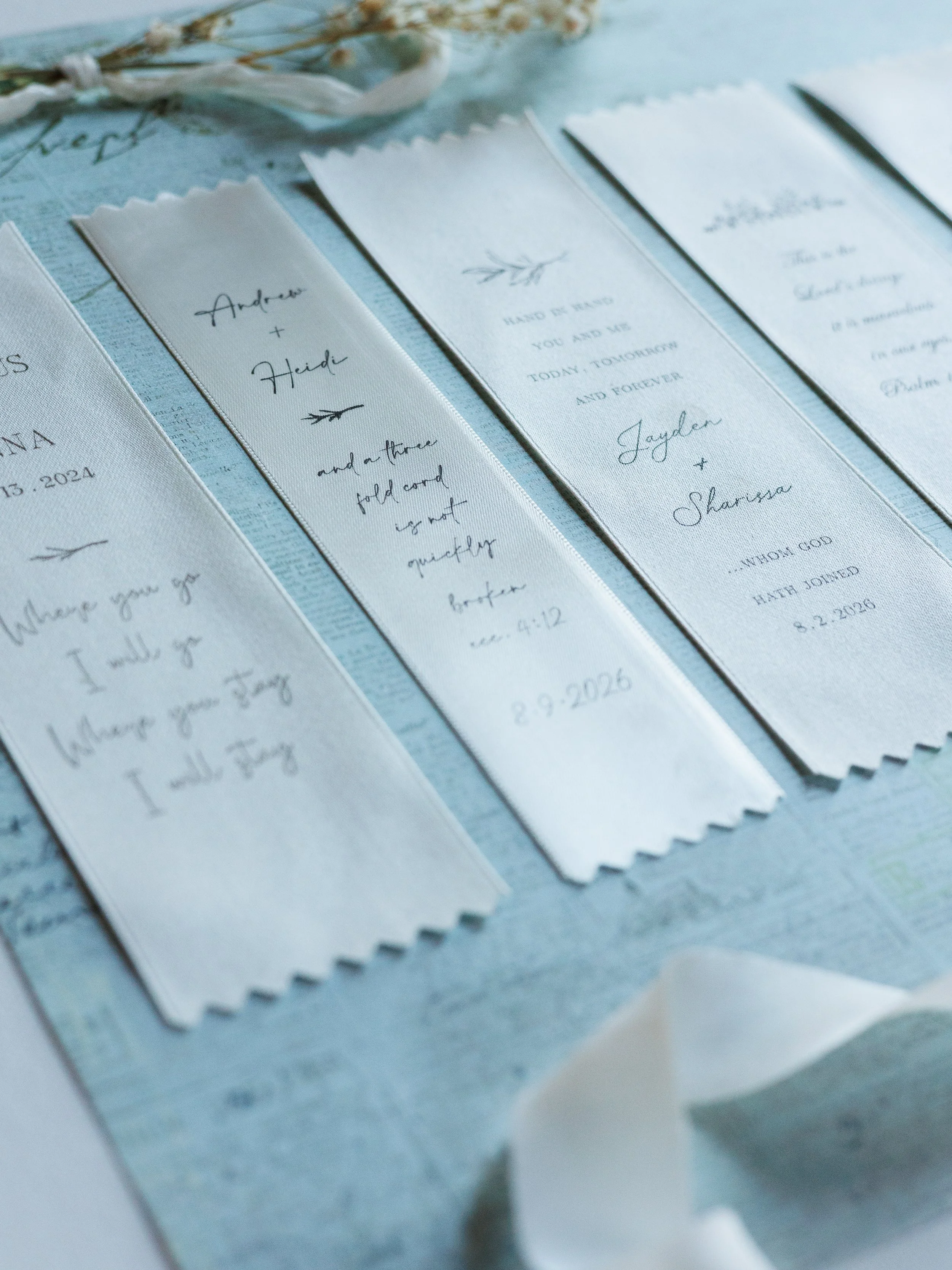 Close-up of wedding programs with handwritten and printed text, decorated with small branch illustrations, on a light blue surface.