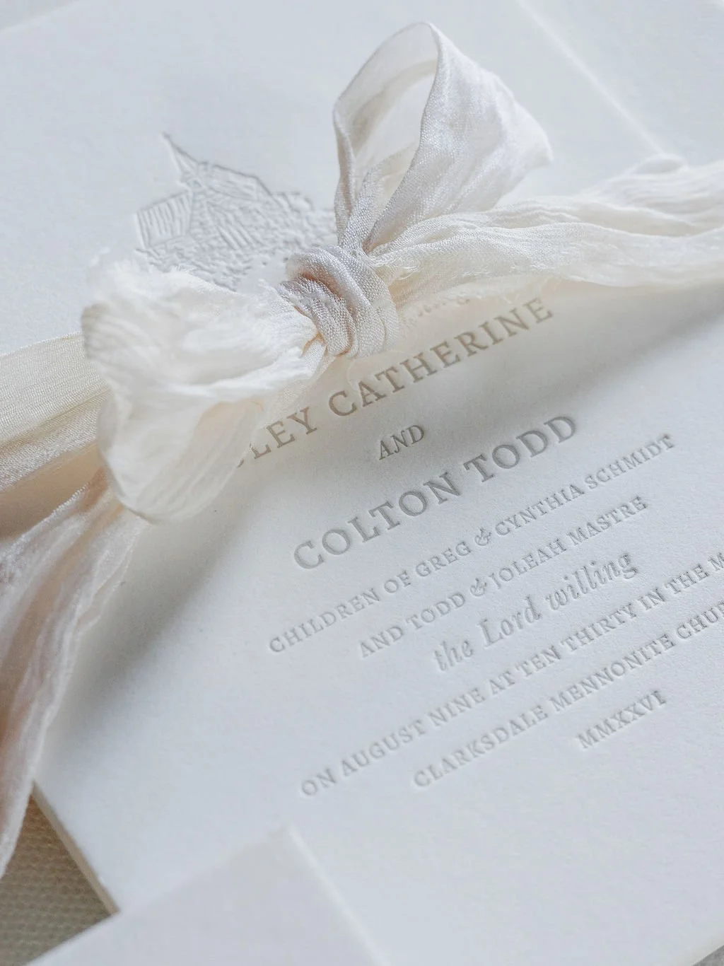 Close-up of wedding invitation with cream-colored ribbon and flower embellishment.
