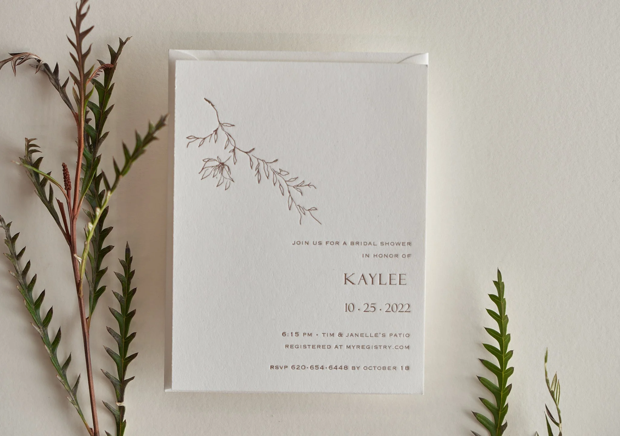 Wedding invitation card with floral illustrations, surrounded by green and brown decorative foliage.