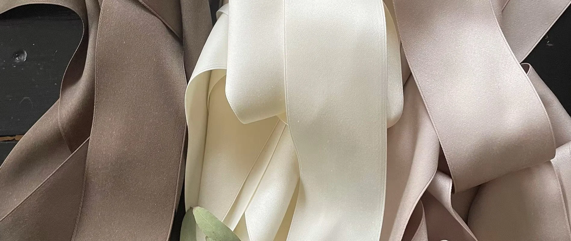 Multiple satin ribbons in shades of cream, beige, and taupe are layered and draped, creating a textured arrangement of fabric strips.