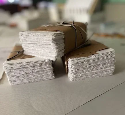 Three stacks of white paper with rough edges, wrapped in brown paper and tied with string.