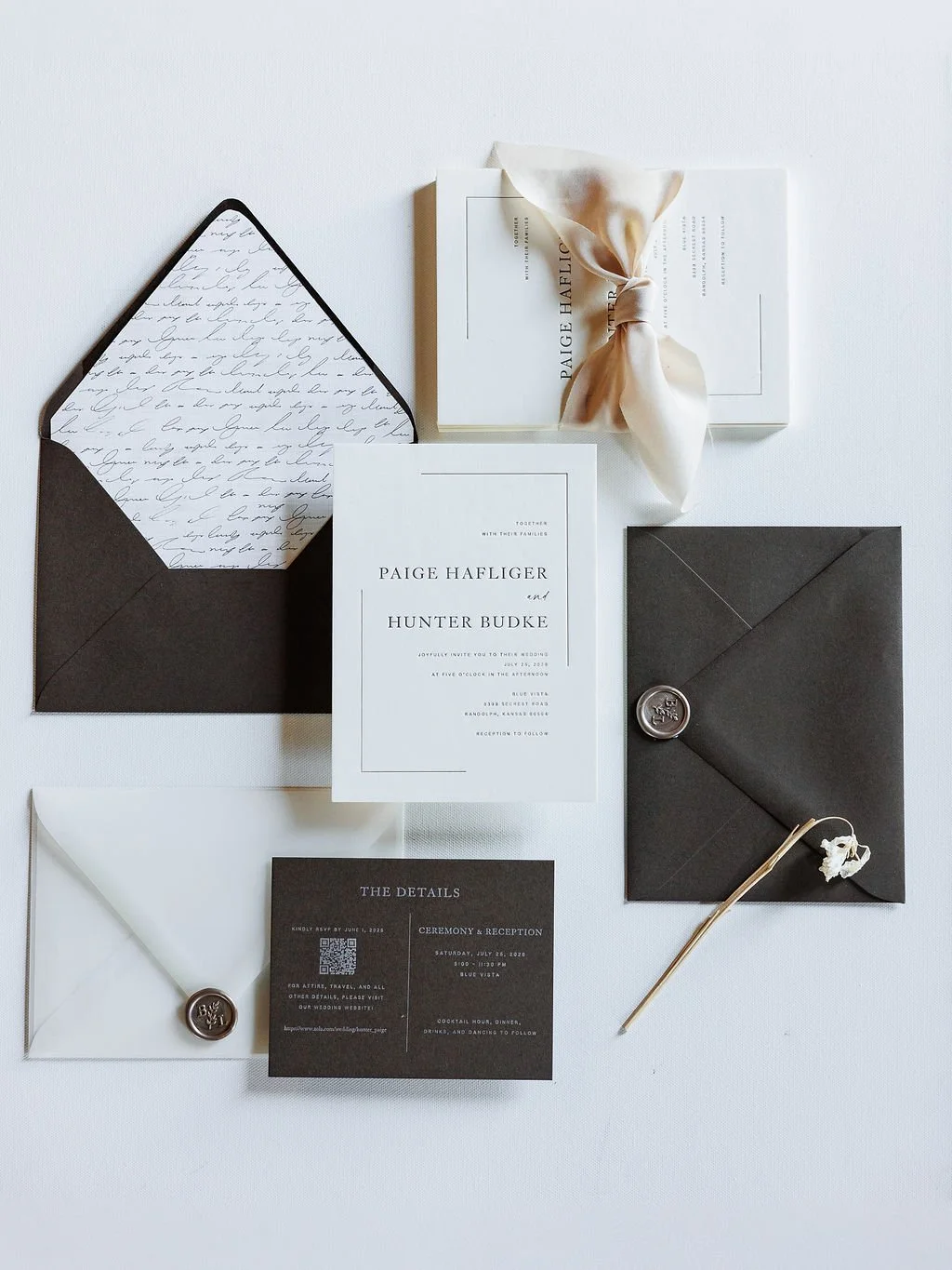 Elegant wedding invitations with black and white designs, including an RSVP card, on a white background with a white ribbon, an open black envelope with handwriting-lined interior, and a black envelope with a wax seal.