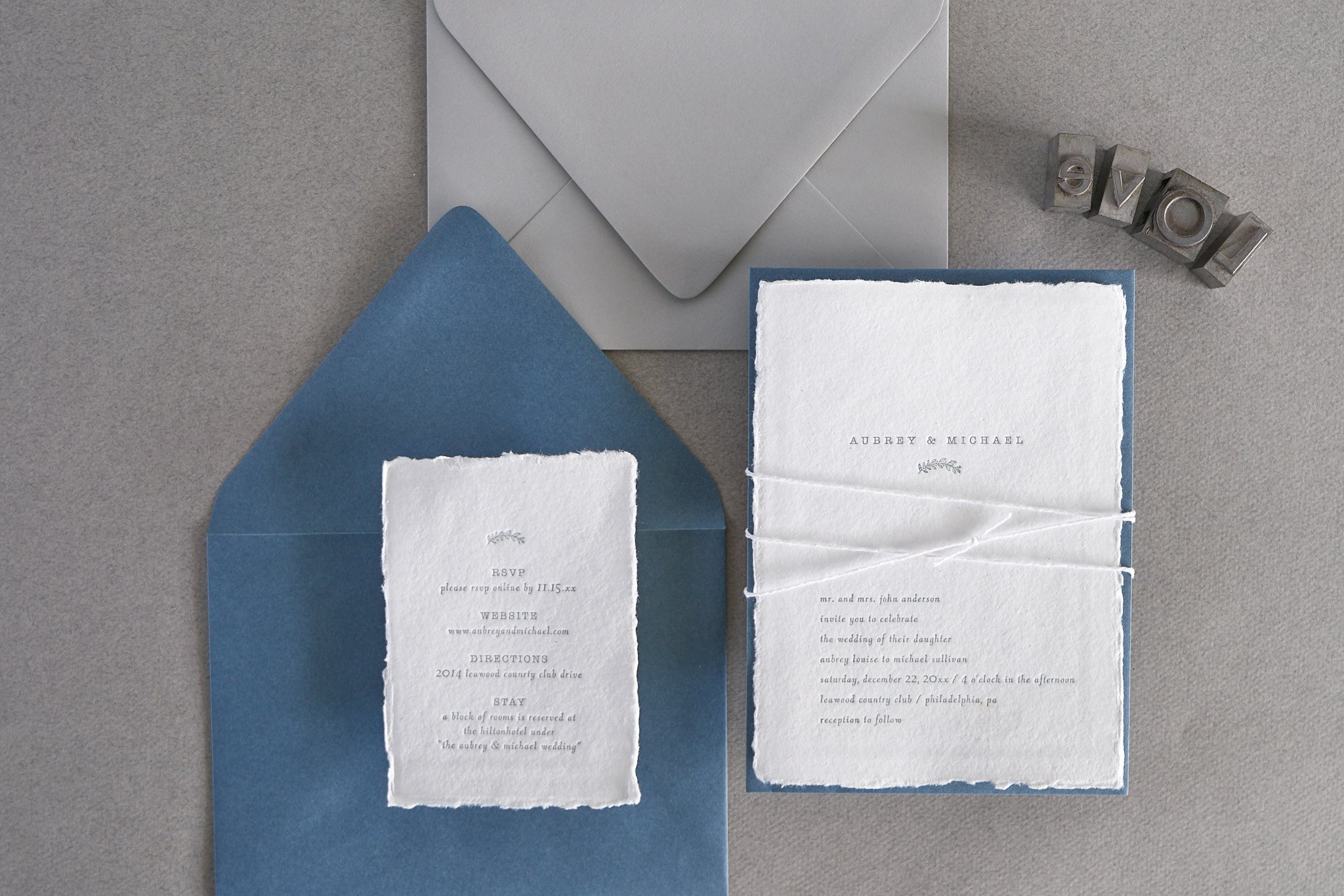 Invitation cards and envelopes for a wedding, with the names Aubrey and Michael, on a gray surface. There are rubber stamps spelling out 'LOVE' in the upper right corner.