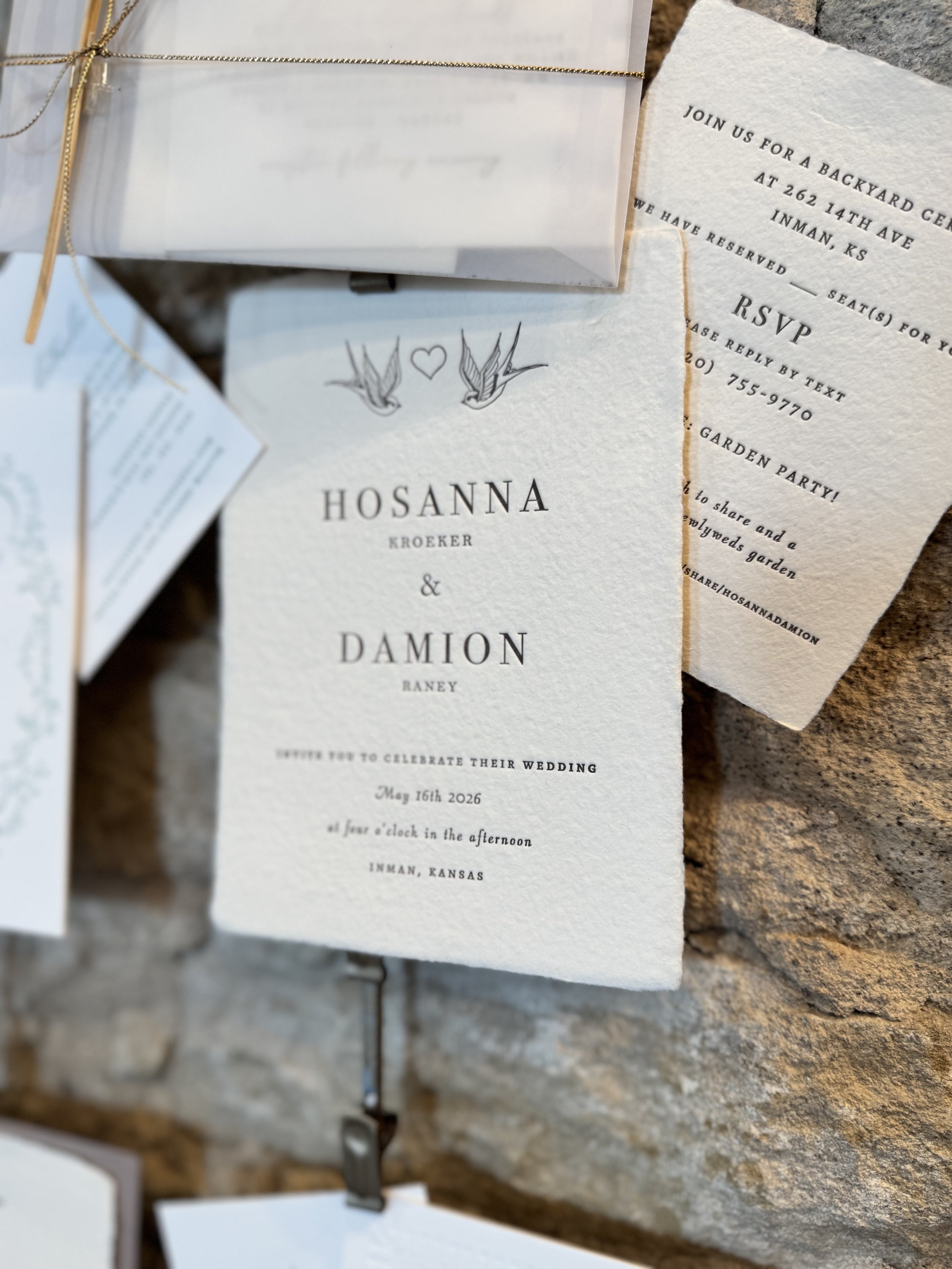 Wedding invitation card with bird illustrations and event details, placed on a textured stone surface.
