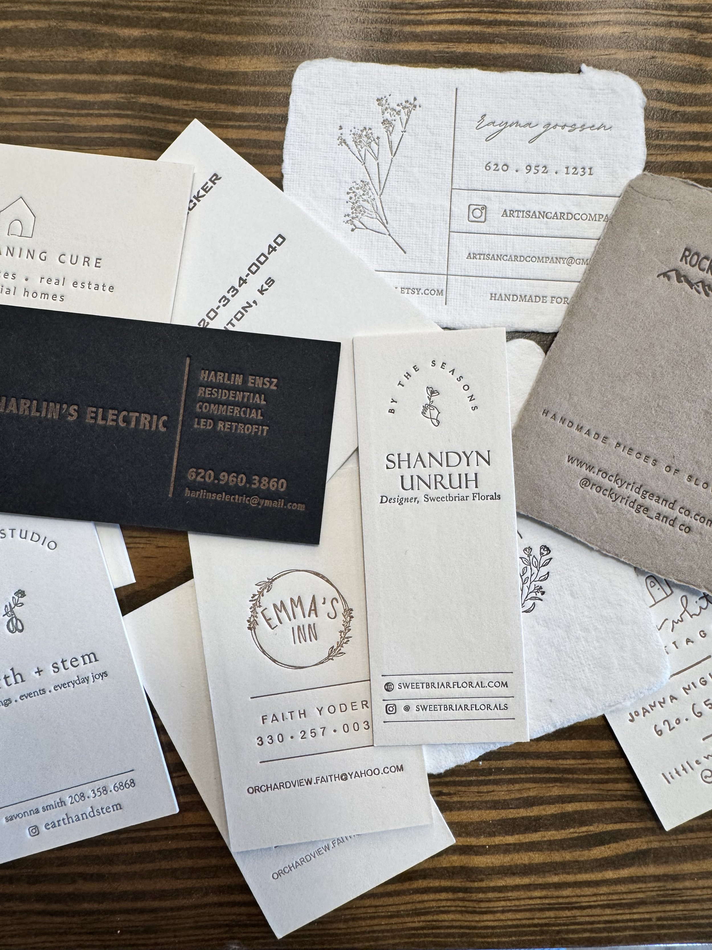 A variety of business cards for different companies and individuals, some with contact information, social media handles, and logos, spread out on a wooden surface.