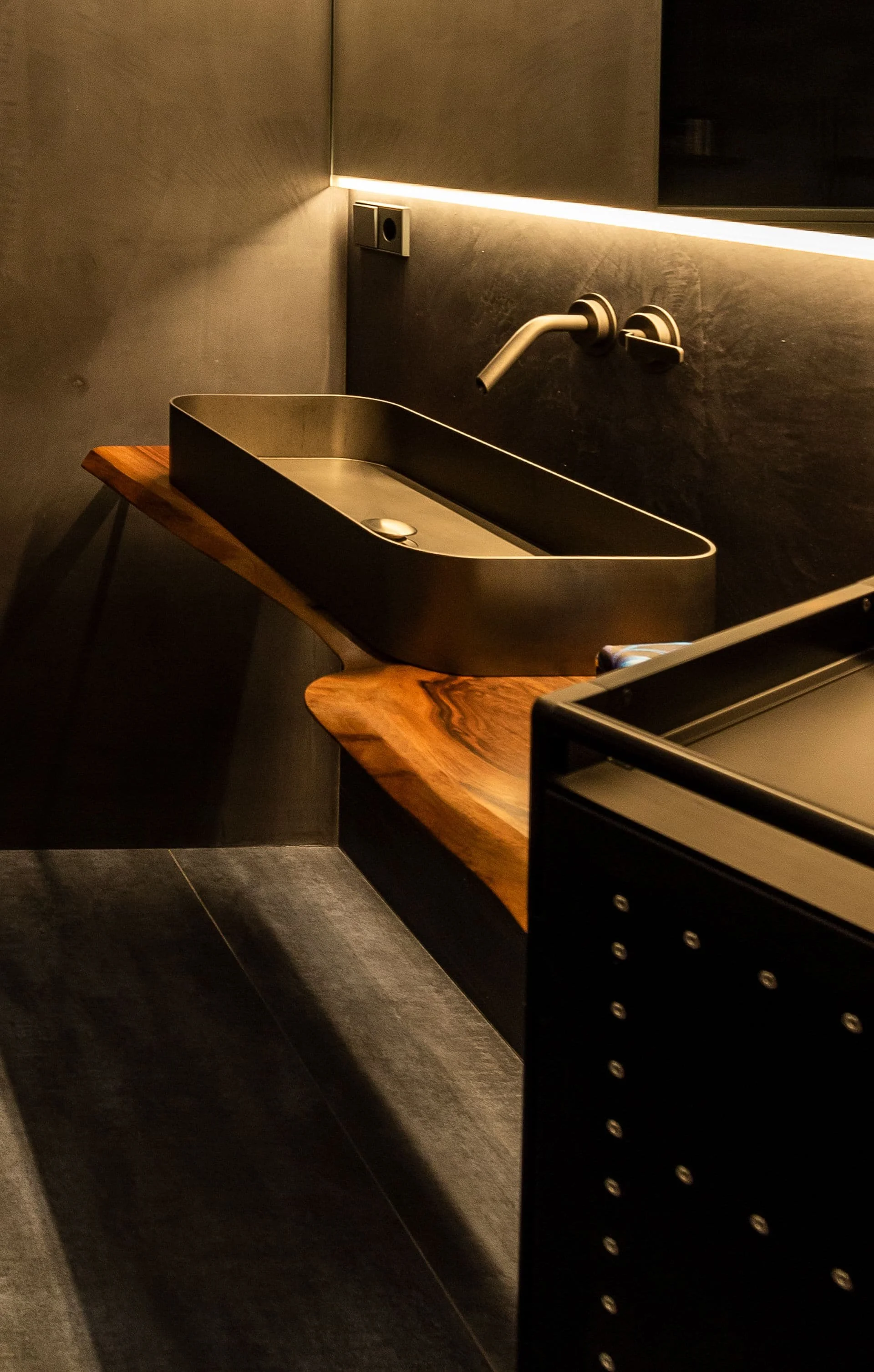 Schwarzer Waschbecken aus Metall auf einem Holztablett, dunkles Mosaik-Wandfliesen und ein moderner Wasserhahn, ambiente Beleuchtung.