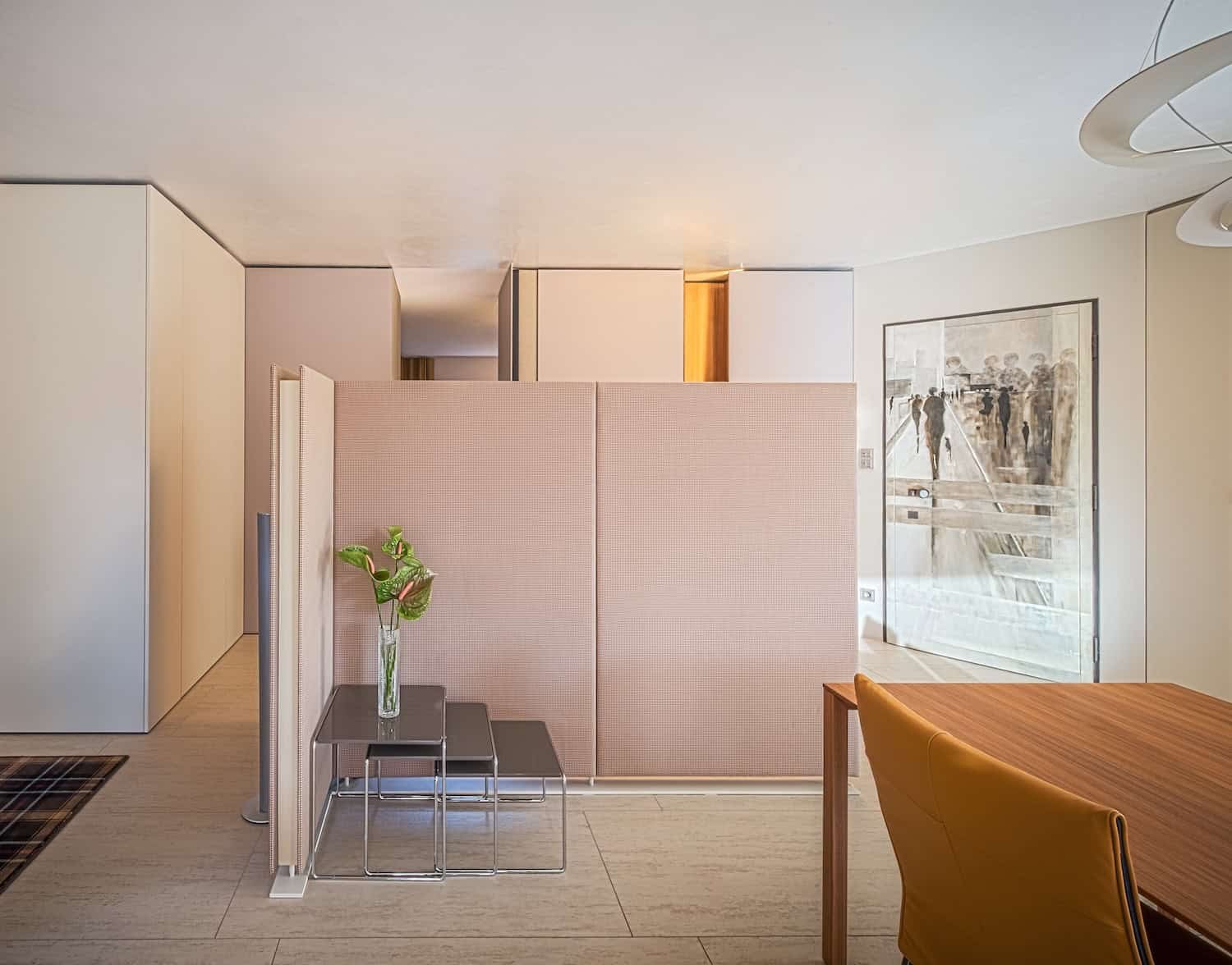 Innenraum eines modernen Apartments mit einer Trennwand, einer Vase mit grünen Blättern, einem Holzschreibtisch und einem goldenfarbenen Stuhl, einer Wand mit Kunstwerk und einer regulären Tür.