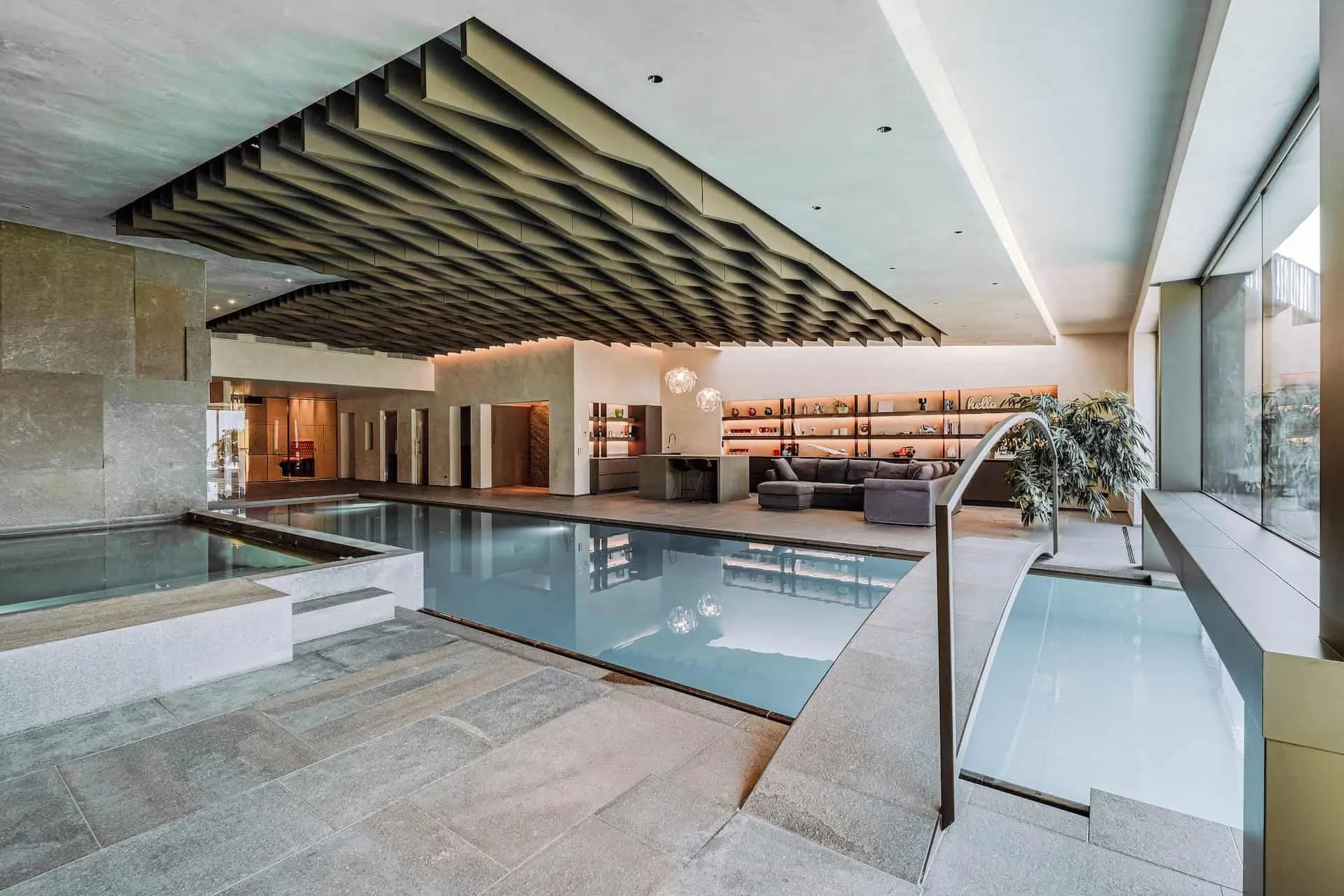 Innenraum eines modernen Wellnesshotels mit Schwimmbad, gemütlicher Sitzecke, Bücherregalen und großen Fenstern mit Aussicht auf die Stadt.