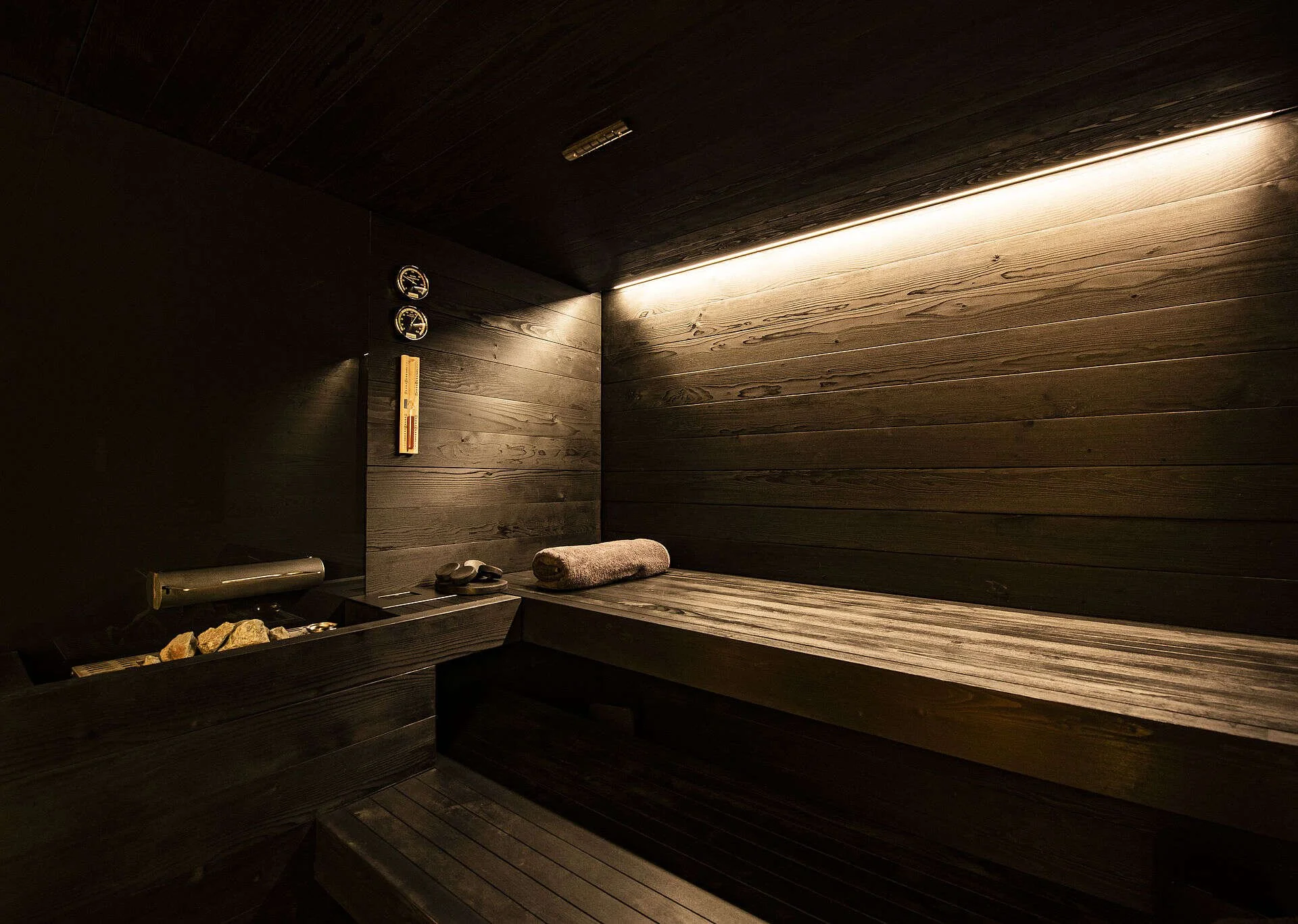 Innenansicht einer dunklen Sauna mit Holzverkleidung, Heizstein und Handtuch auf einer Bank