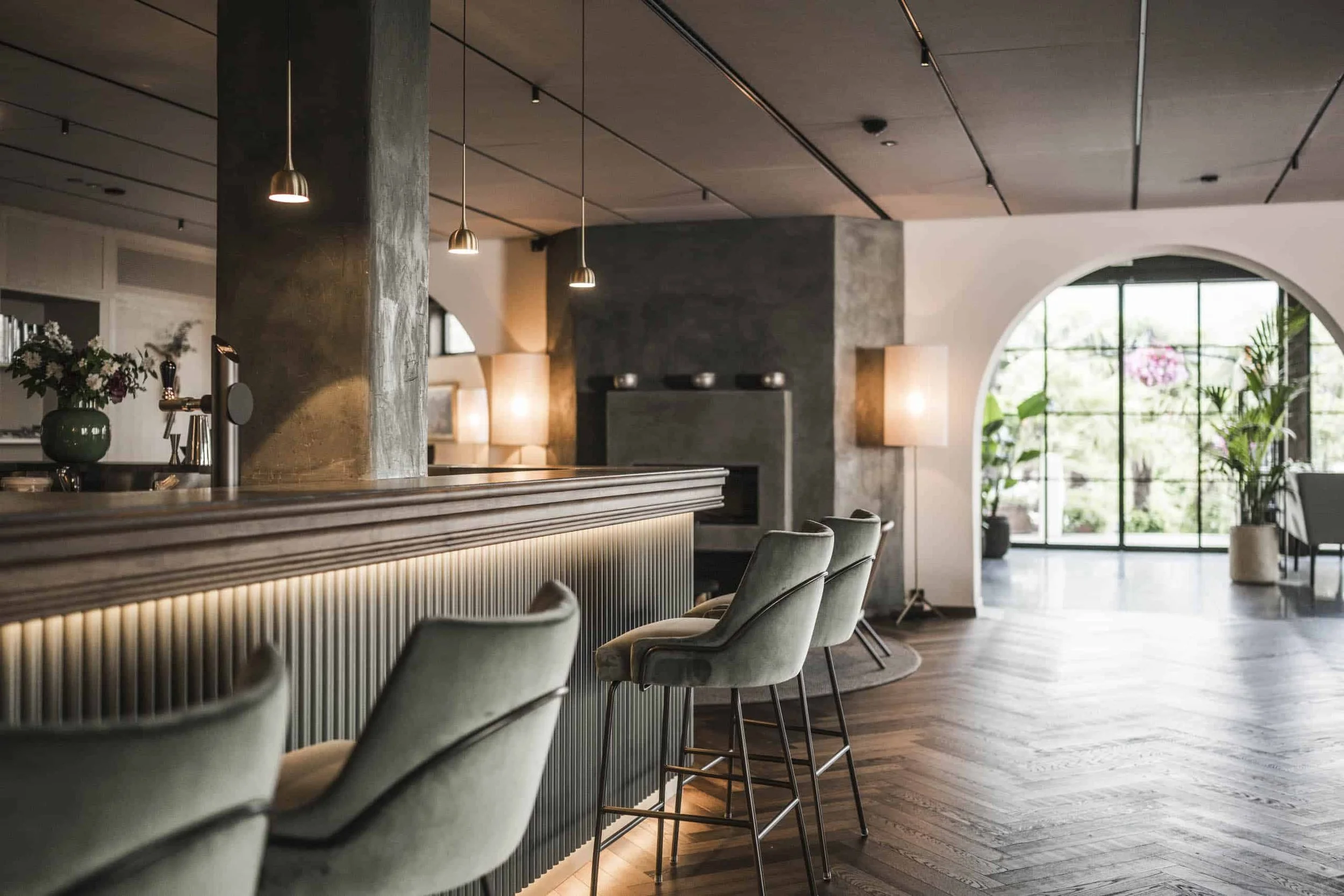 Ein elegantes, modernes Hotelrestaurant mit einem langen Thekenbereich, bequemen Stühlen und großen Fenstern, die viel Tageslicht und Pflanzen im Hintergrund bringen.