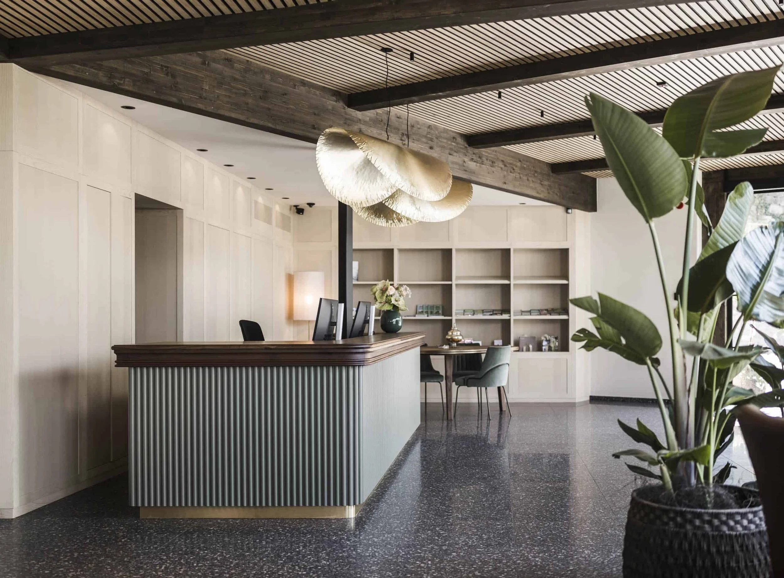 Innenraum eines modernen, stilvollen Hotels oder Restaurants mit Empfangstresen, Hockern, einem Blumenarrangement, einer großen Pflanze und einer Deckenleuchte.