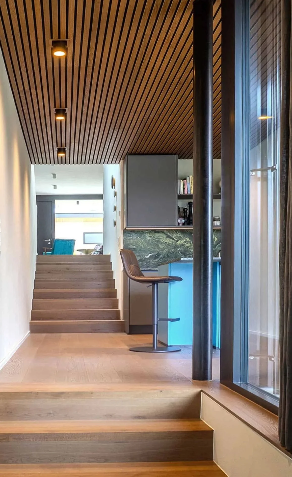 Innenansicht eines modernen Hauses mit Treppen, Holzdecke, einem Stuhl, eine Bar, Bücherregale und großen Fenster