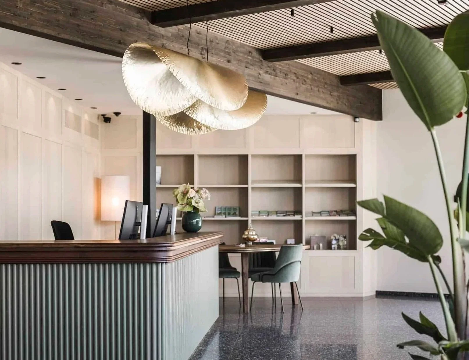 Moderne Hotellobby mit Empfangstresen, großen goldenen Deckenleuchten, Bücherregalen und Sitzgelegenheiten mit Blumenvasen.