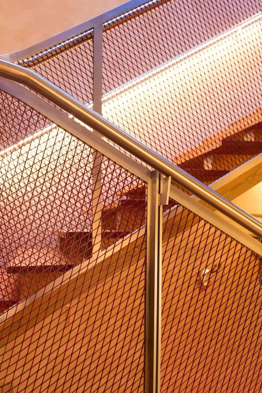 Blick auf eine moderne Treppe mit roten Metallgeländern und einer silbernen Handläufe innen in einem Gebäude.