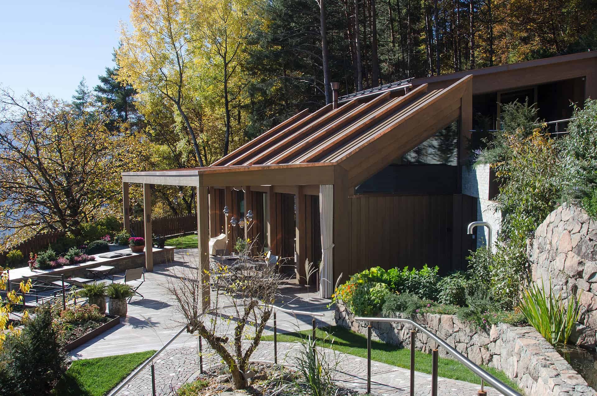 Ein moderner Hausgarten mit Terrasse, Holzdecke, Pflanzen, Bäumen und einer umgebenden Natur im Herbst.