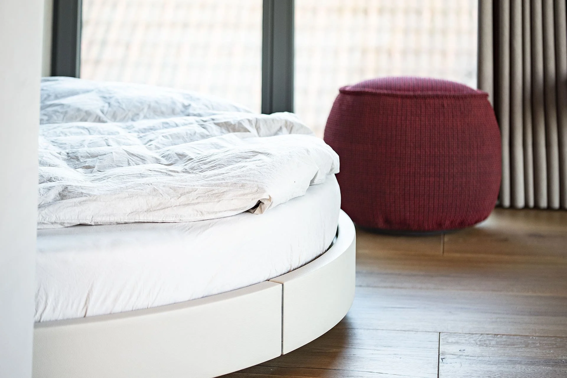 Bett mit weißer Bettwäsche, roter, runder Sitzsack neben einem großen Fenster mit Sicht auf den Himmel.