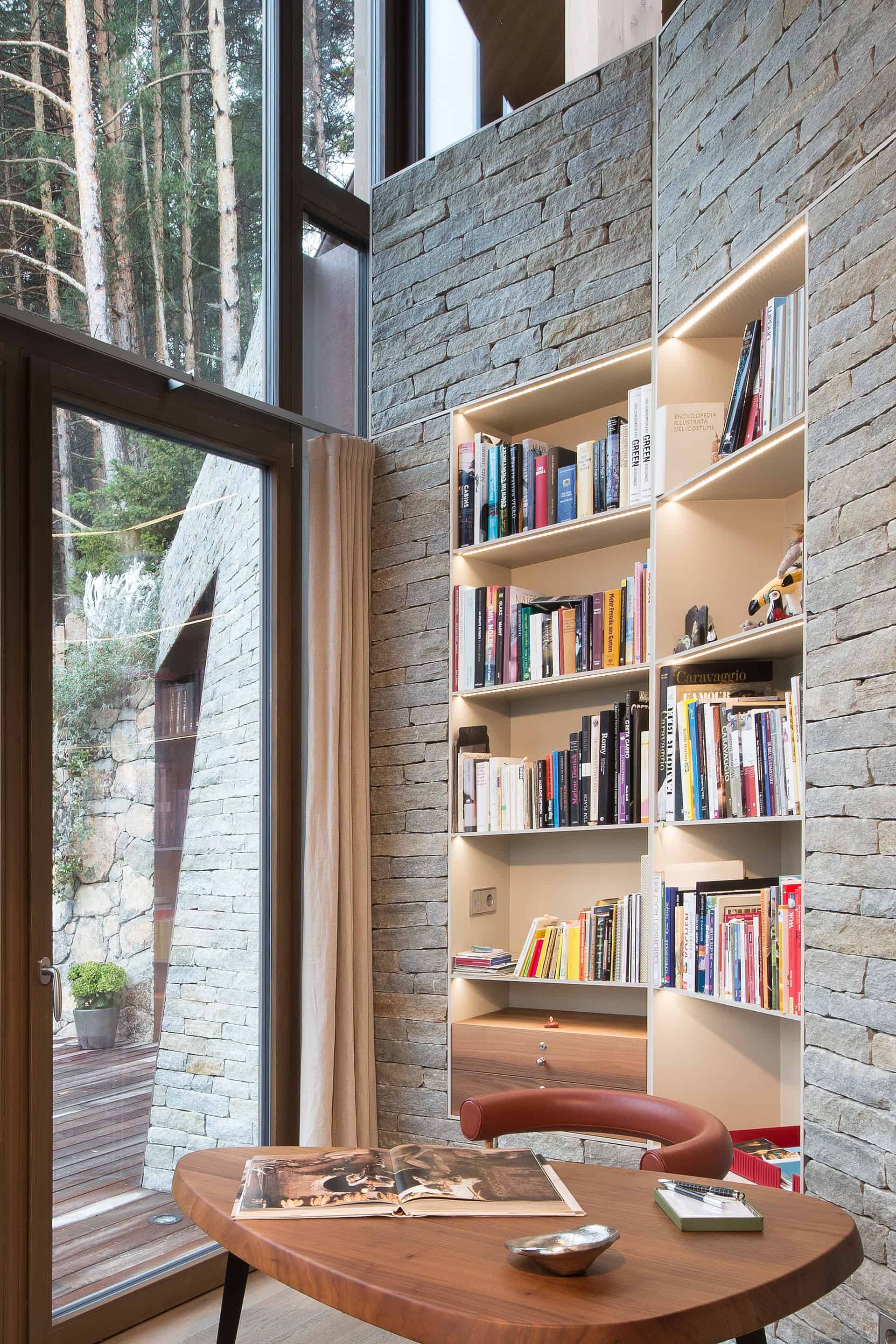Ein modernes Wohnzimmer mit großen Fenstern, einer Bücherwand und einem runden Holztisch.