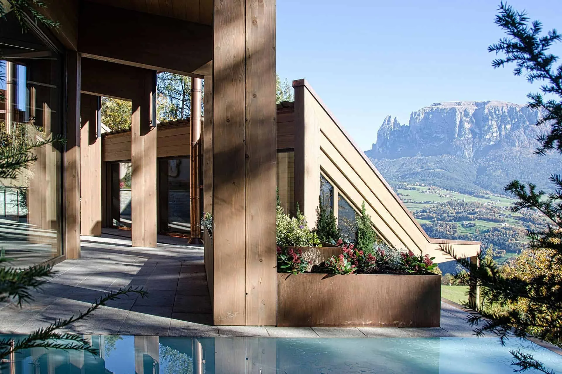 Moderne Holzarchitektur mit Bergblick, Balkon mit Blumenschmuck und Pool im Vordergrund.