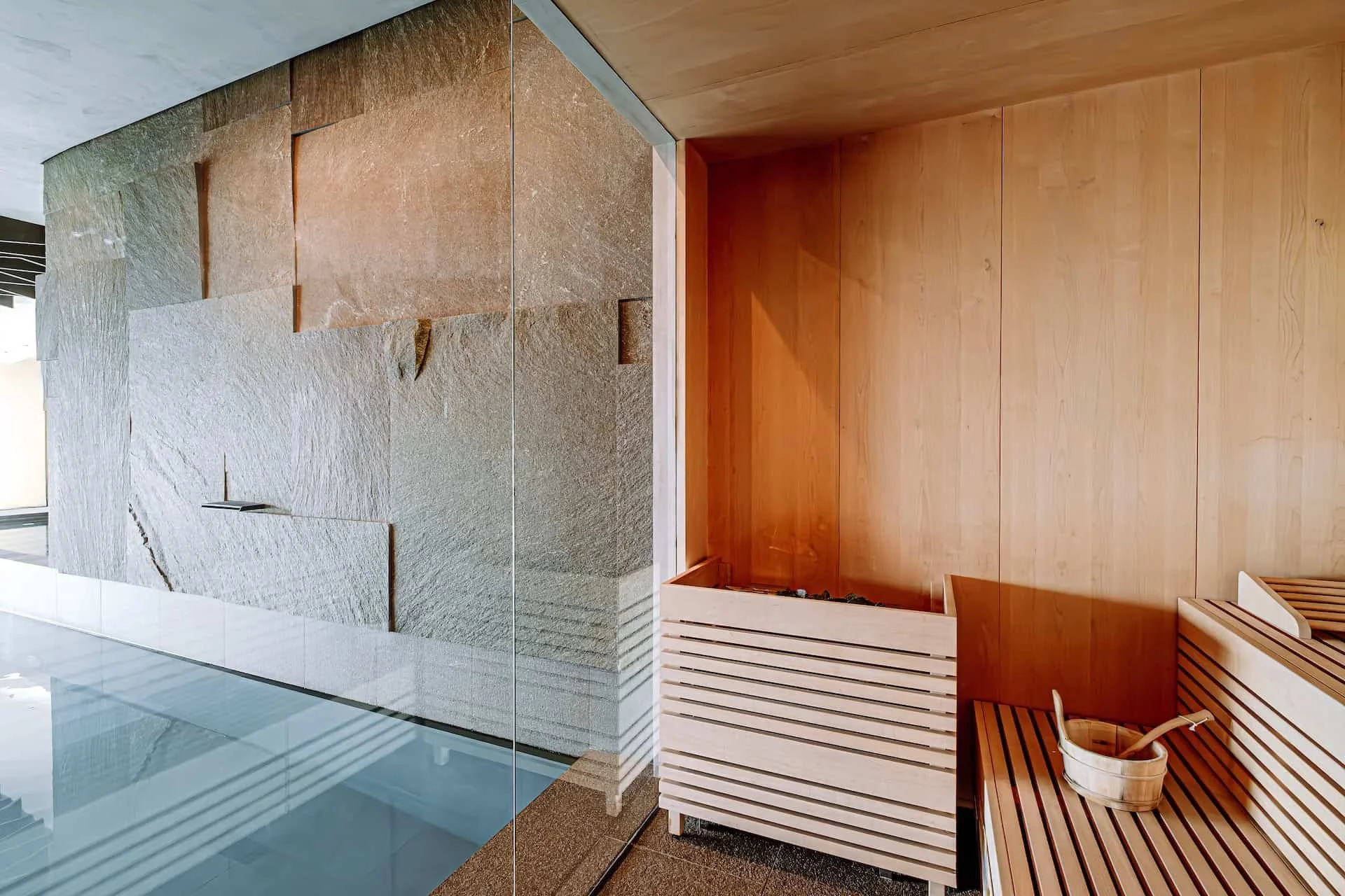 Innenraum mit einer Steindecke, Holzverkleidungen und einem Sauna-Bereich mit Holzbank, einem Eimer und Saunahandtuch.