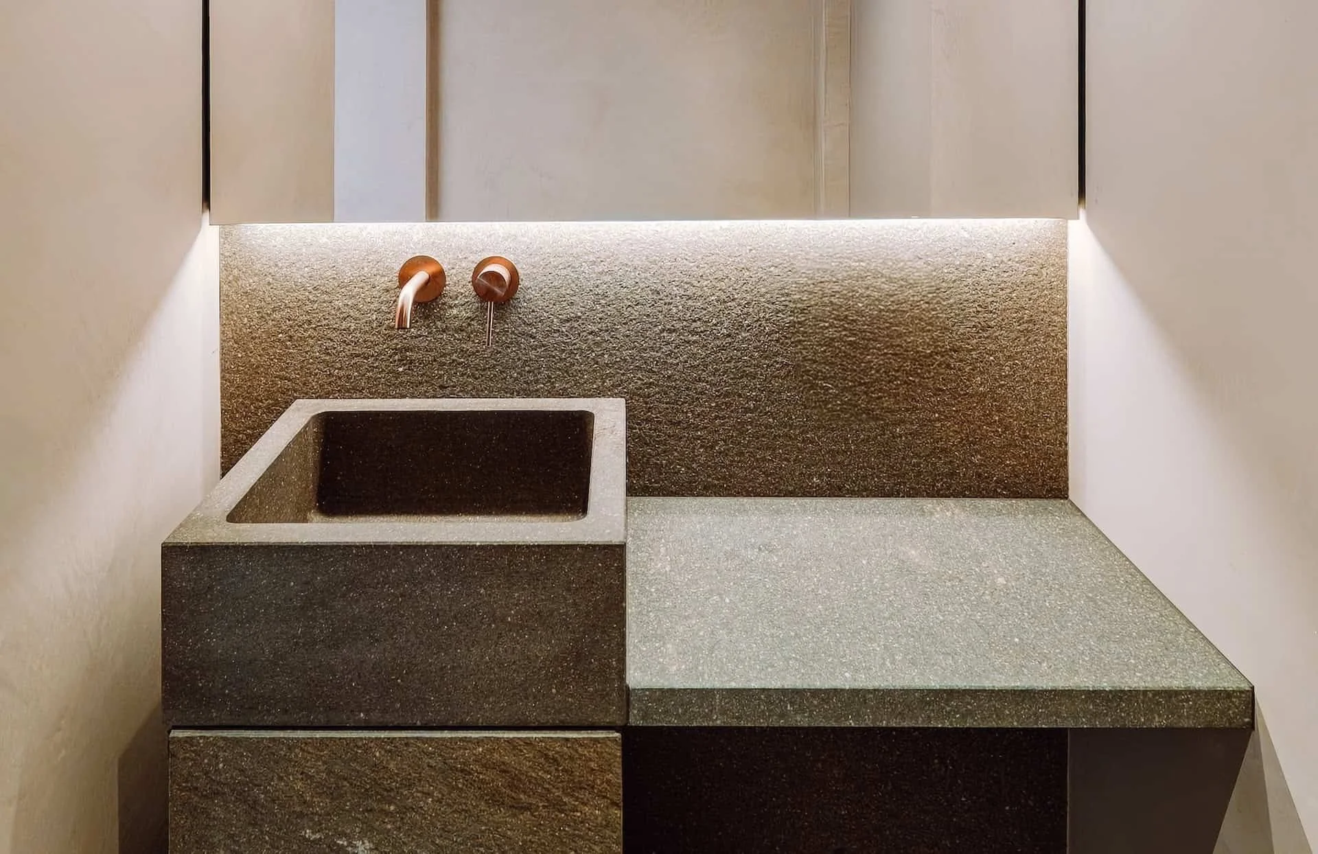 Ein moderner Wasserhahn über einem schwarzen Spülbecken an einer Wand mit grauem Mosaikstein-Design und einem großen Spiegel.